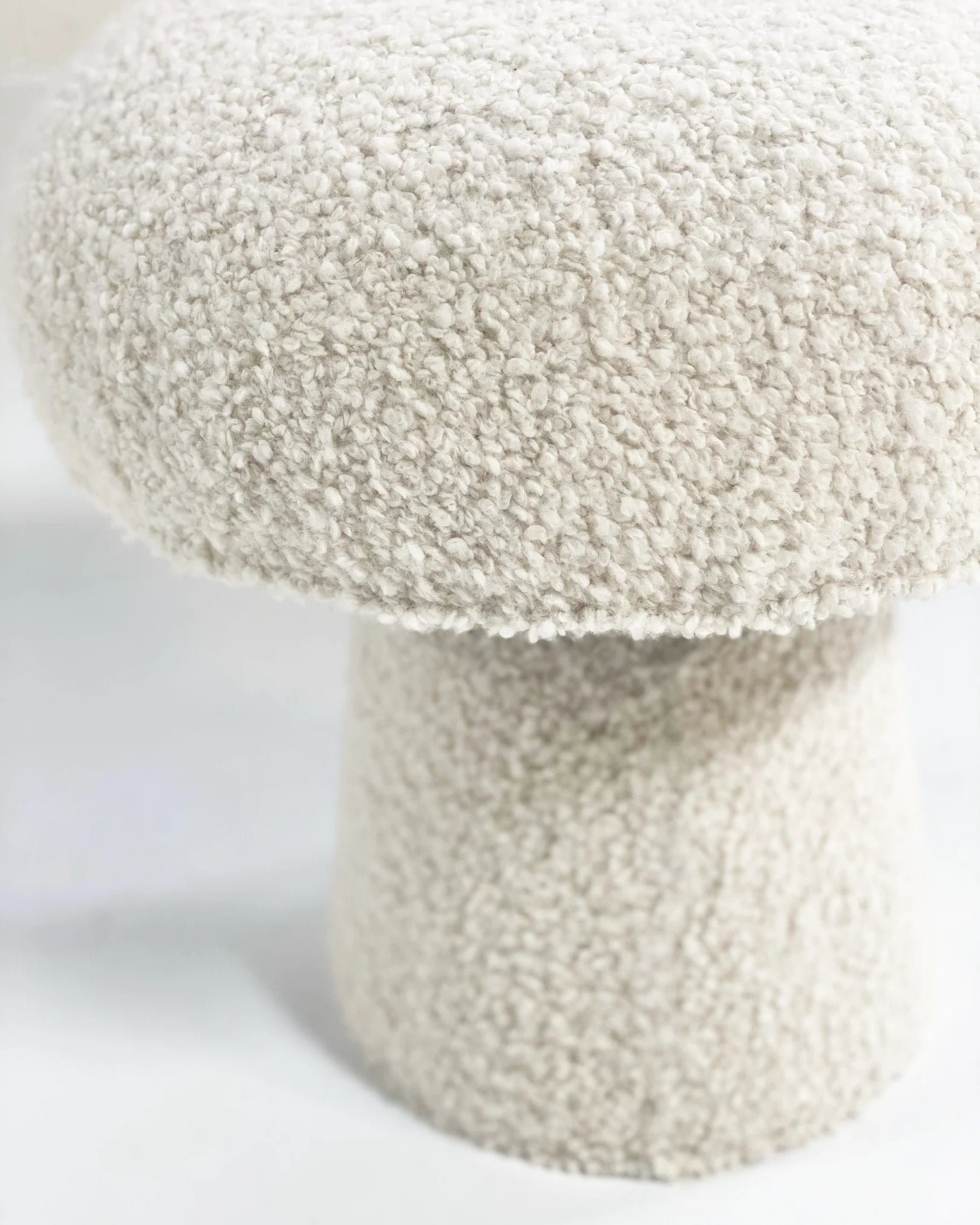 A close-up of The Forsyth Mushroom Pouf in Boucle features a plush, cream-colored, rounded top and cylindrical base, both wrapped in soft boucle fabric.
