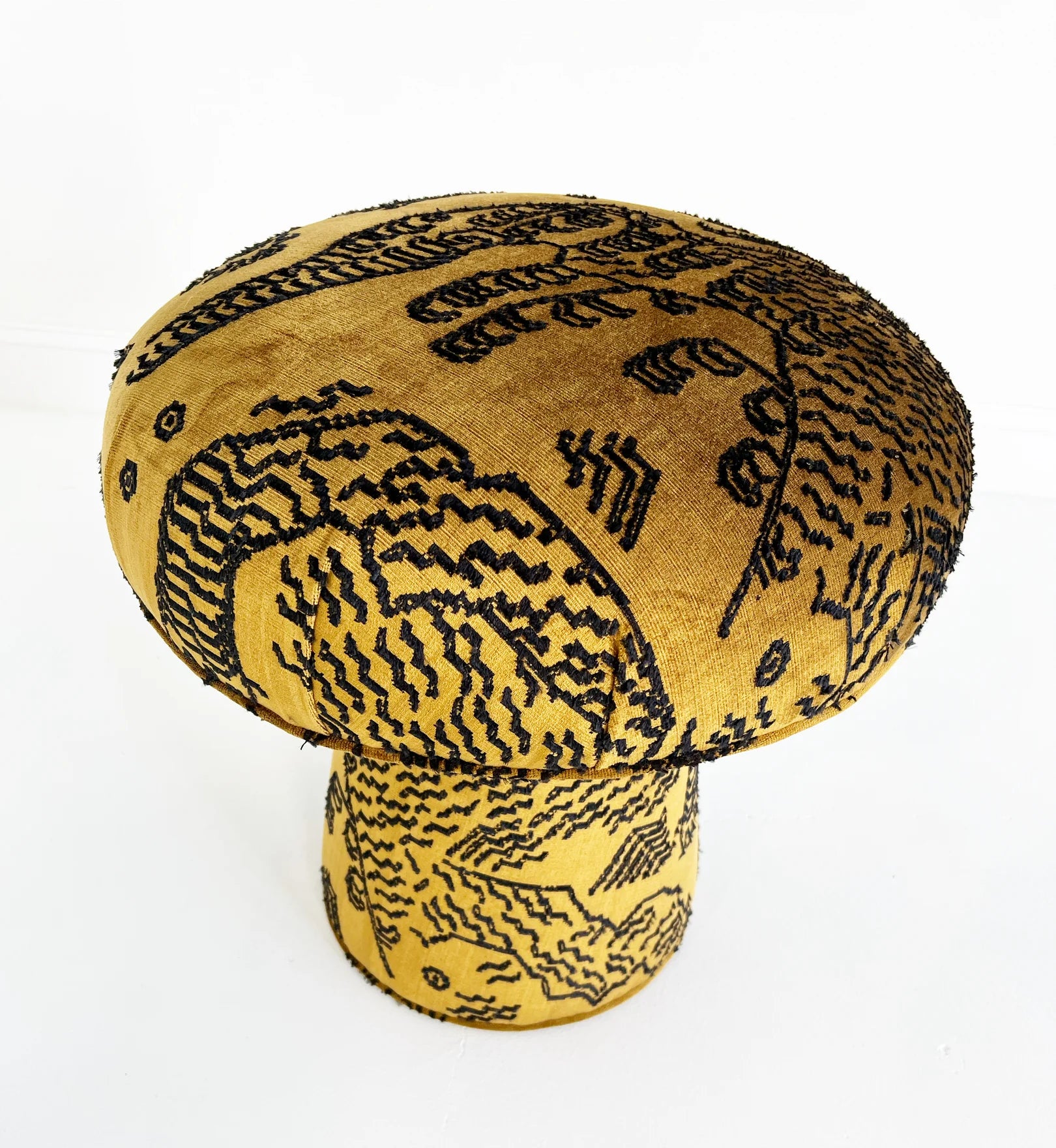 The Forsyth Mushroom Pouf in Dedar 'Tiger Mountain' Jacquard Velvet features a round, mushroom shape with a yellow base and abstract black patterns atop plush velvet, shown on a white surface.