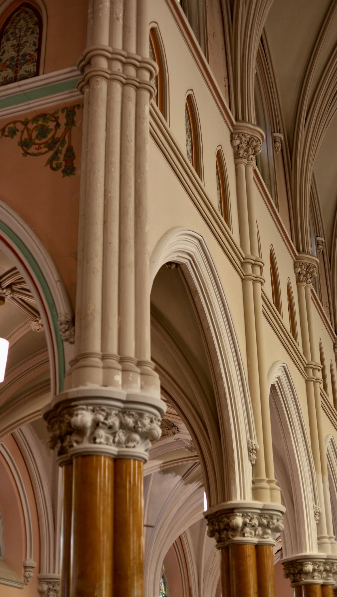 A close-up view of ornate, arched columns inside a historic church or cathedral, featuring decorative capitals and intricate architectural details in warm beige and brown tones.