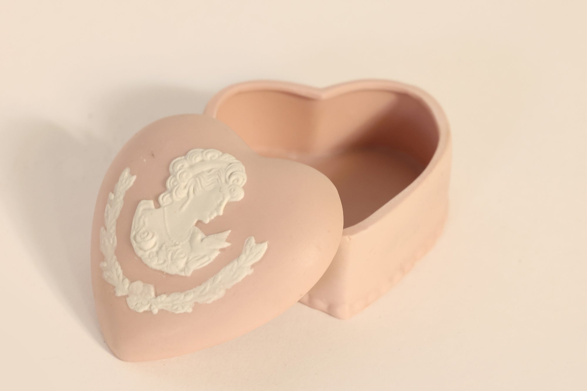 The Vintage Jasperware Style Heart Trinket Box by Euro Trash Annie, in pale pink with classical white cameo relief, sits slightly open on a light background.