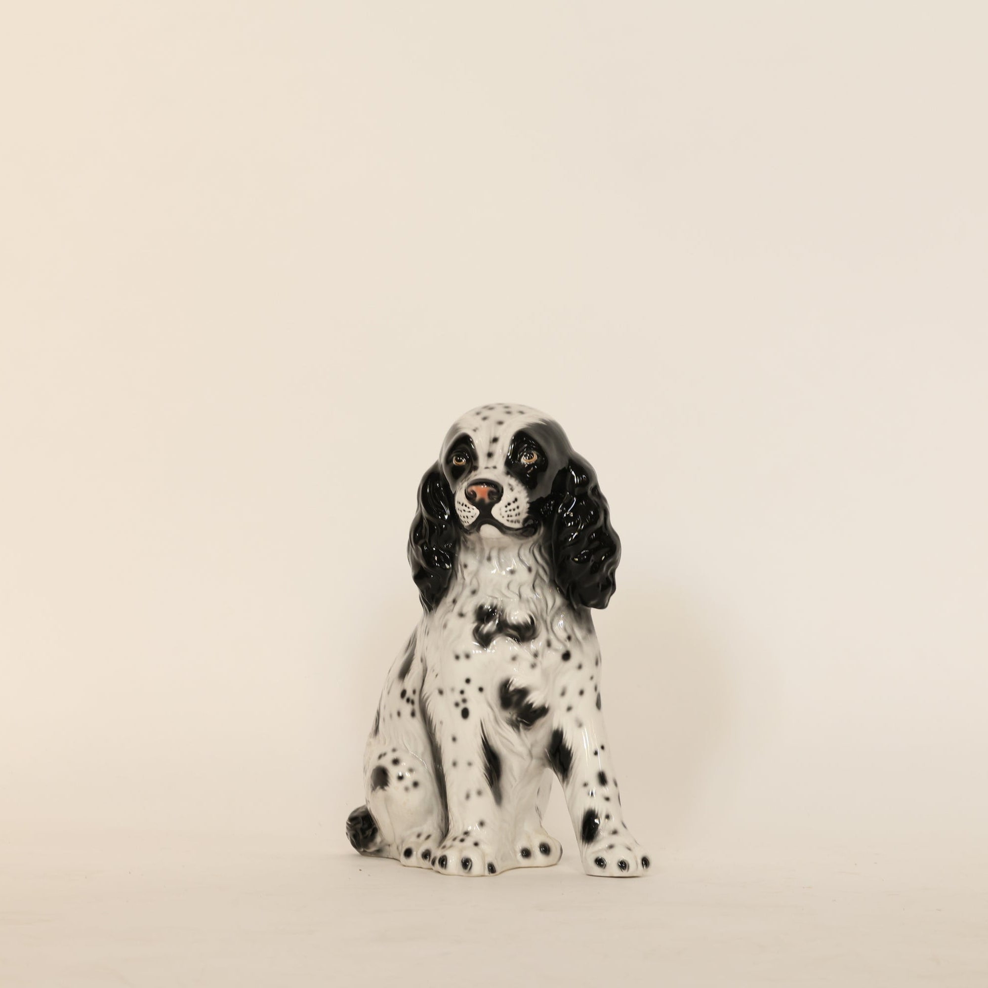 Ceramic dog figurine with black and white spots on a beige background