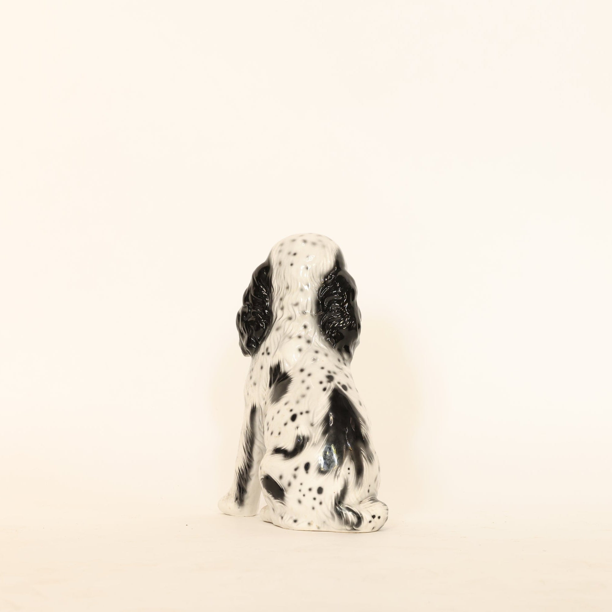 Small ceramic dog figurine with black spots on a beige background