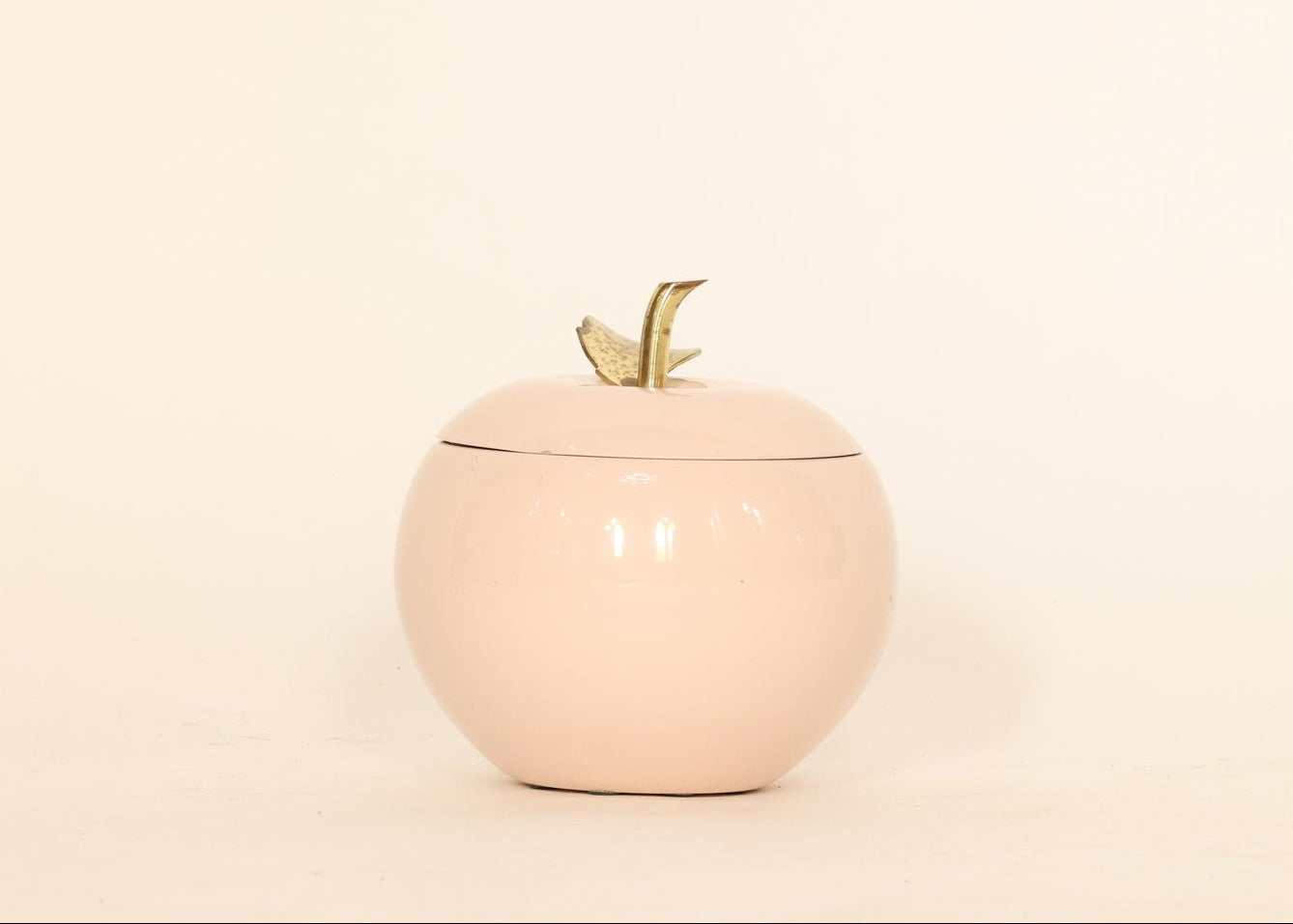 Pink apple-shaped container with a gold leaf on a beige background