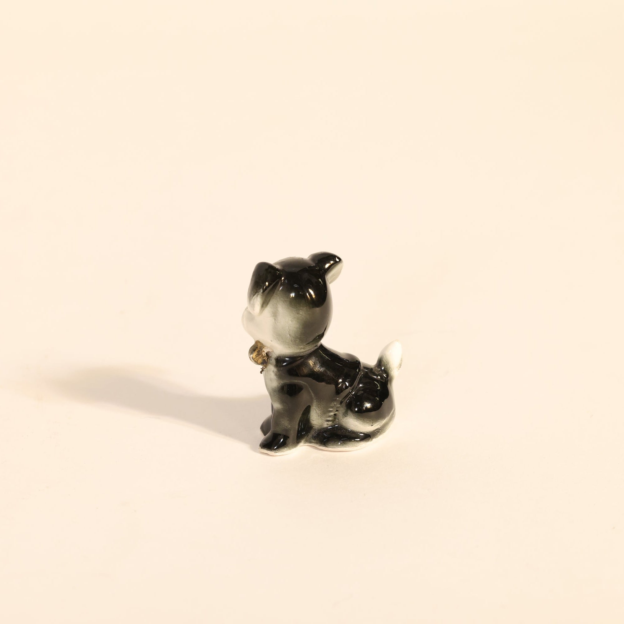 Small black and white ceramic dog figurine on a beige background