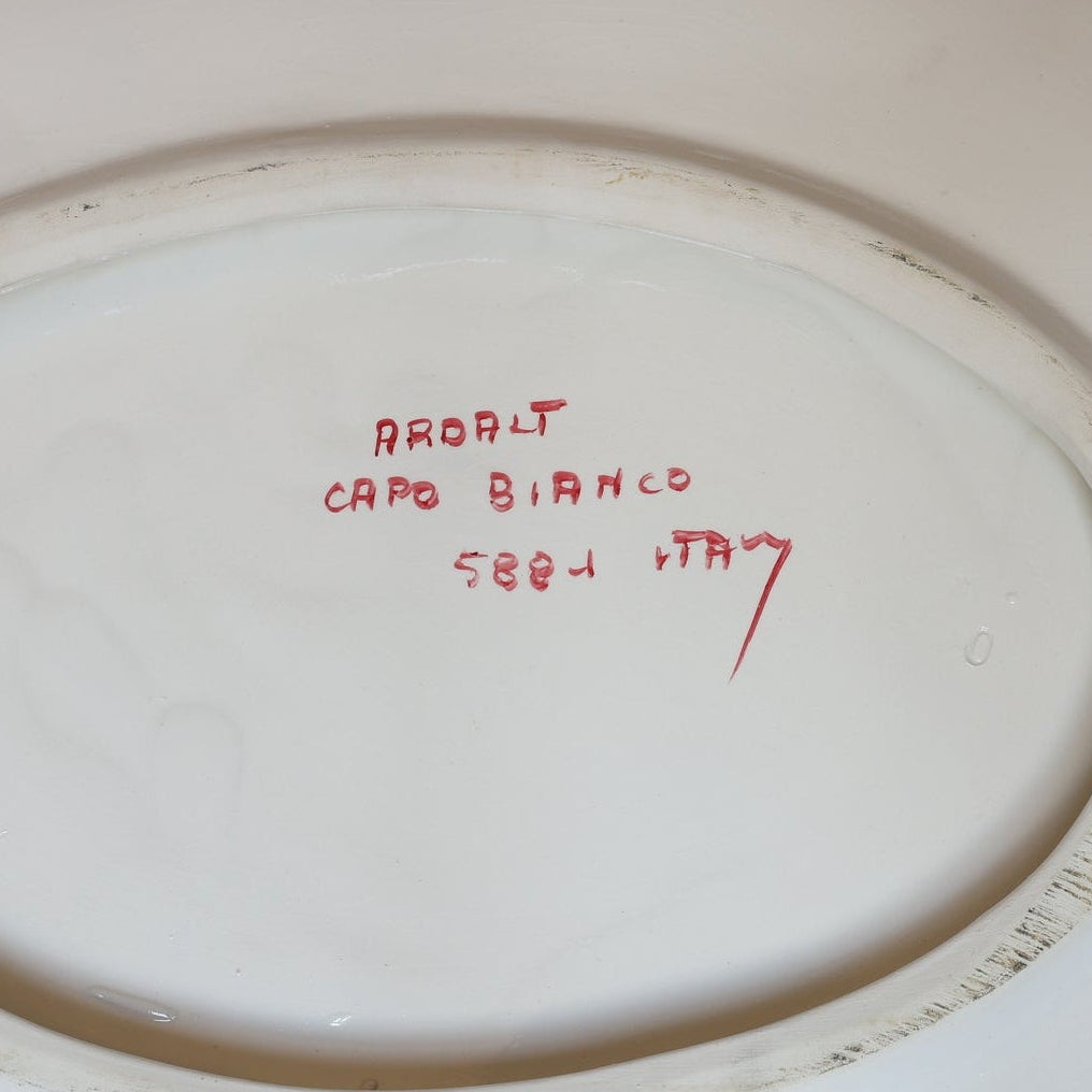 The underside of this Euro Trash Vintage White Ceramic Tureen with Underplate and Ladle features handwritten red text, "AROLAT CAPO BIANCO 7883 ITALY," within an oval unglazed area.