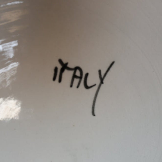 The Euro Trash Vintage White Ceramic Cherub Shell Dish features "Italy" handwritten in black ink. Light reflects off the glossy surface, making it ideal as a trinket holder or decorative centerpiece.