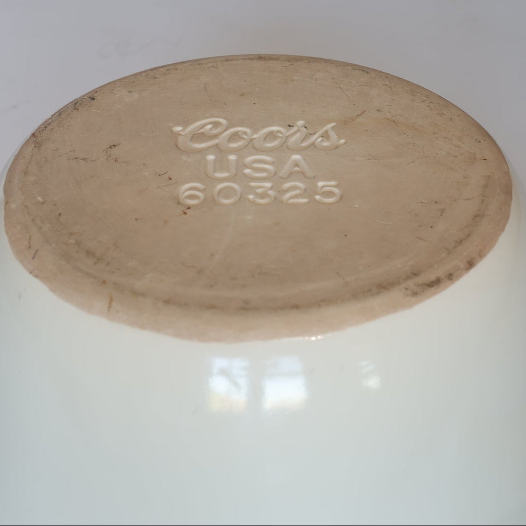 The base of the Vintage White Ceramic Mortar and Pestle Set by Euro Trash is shown, displaying embossed Coors USA 60325. The worn, discolored surface reflects its collectible decorative kitchenware status.