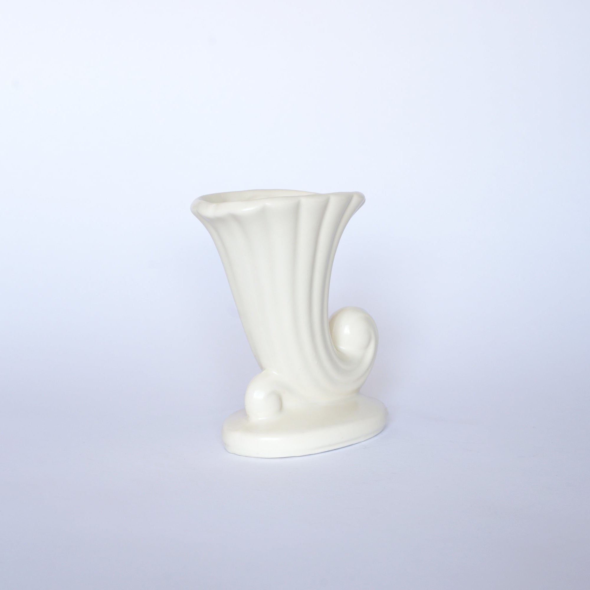 The Euro Trash Vintage White Cornucopia Ceramic Vase features a fluted, horn-like design with a curled base, making it a striking decorative accent against any plain light background.