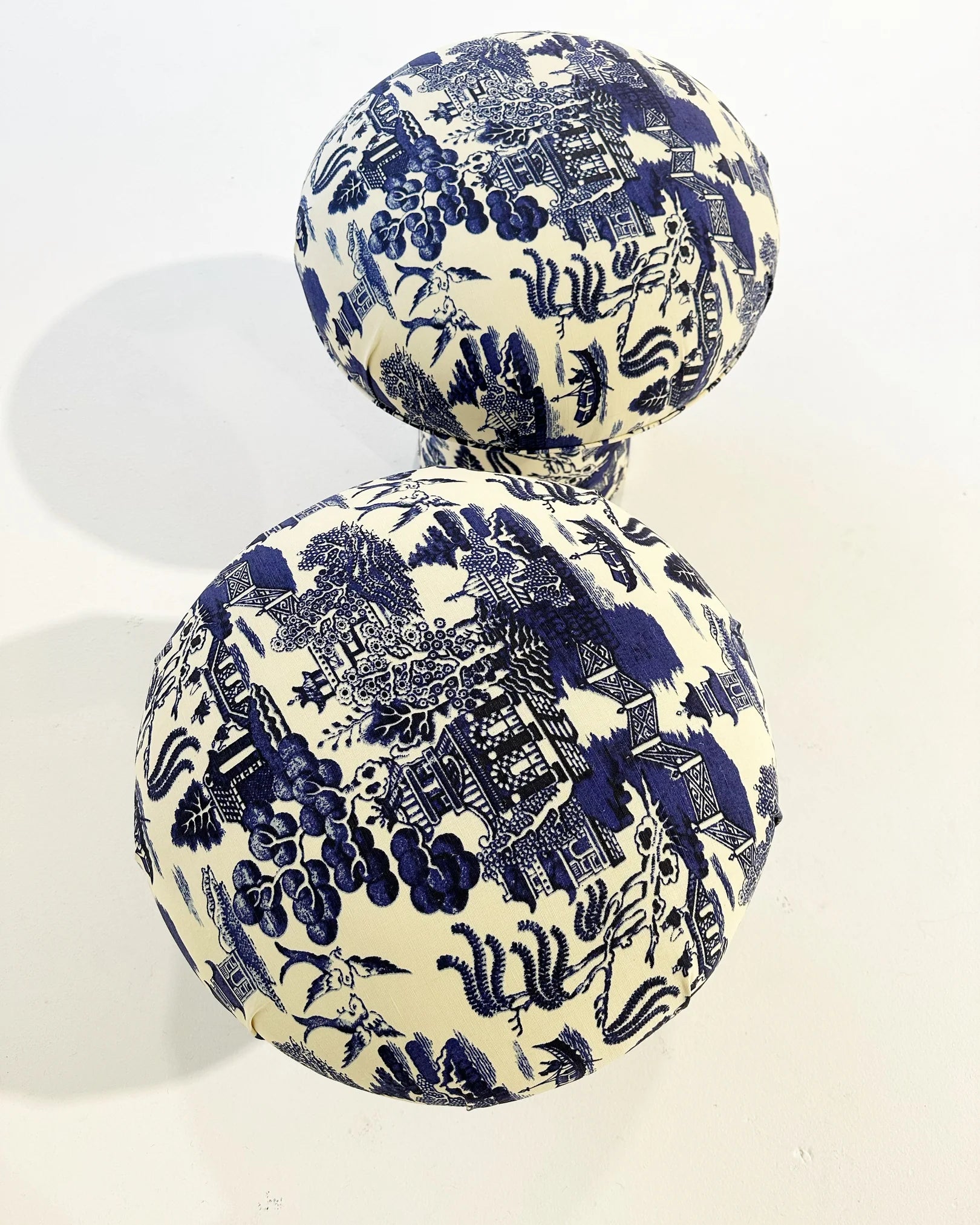 Two round handmade ottomans in Beata Heuman Willow Linen Cotton from The Forsyth Mushroom Pouf collection, featuring blue and white toile-inspired scenes—an enchanting accent with whimsical charm for any space.