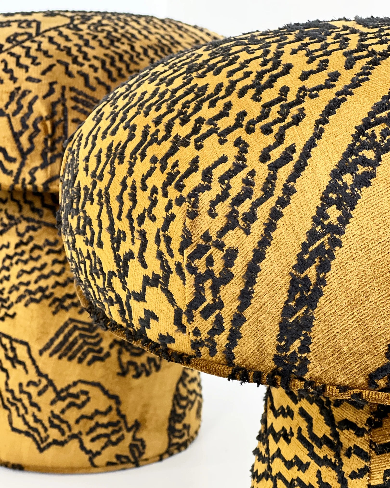 Close-up of two Forsyth Mushroom Poufs in Dedar 'Tiger Mountain' jacquard velvet, featuring yellow fabric with bold black patterns. The white background accentuates the abstract, intricate designs on each unique handmade ottoman.