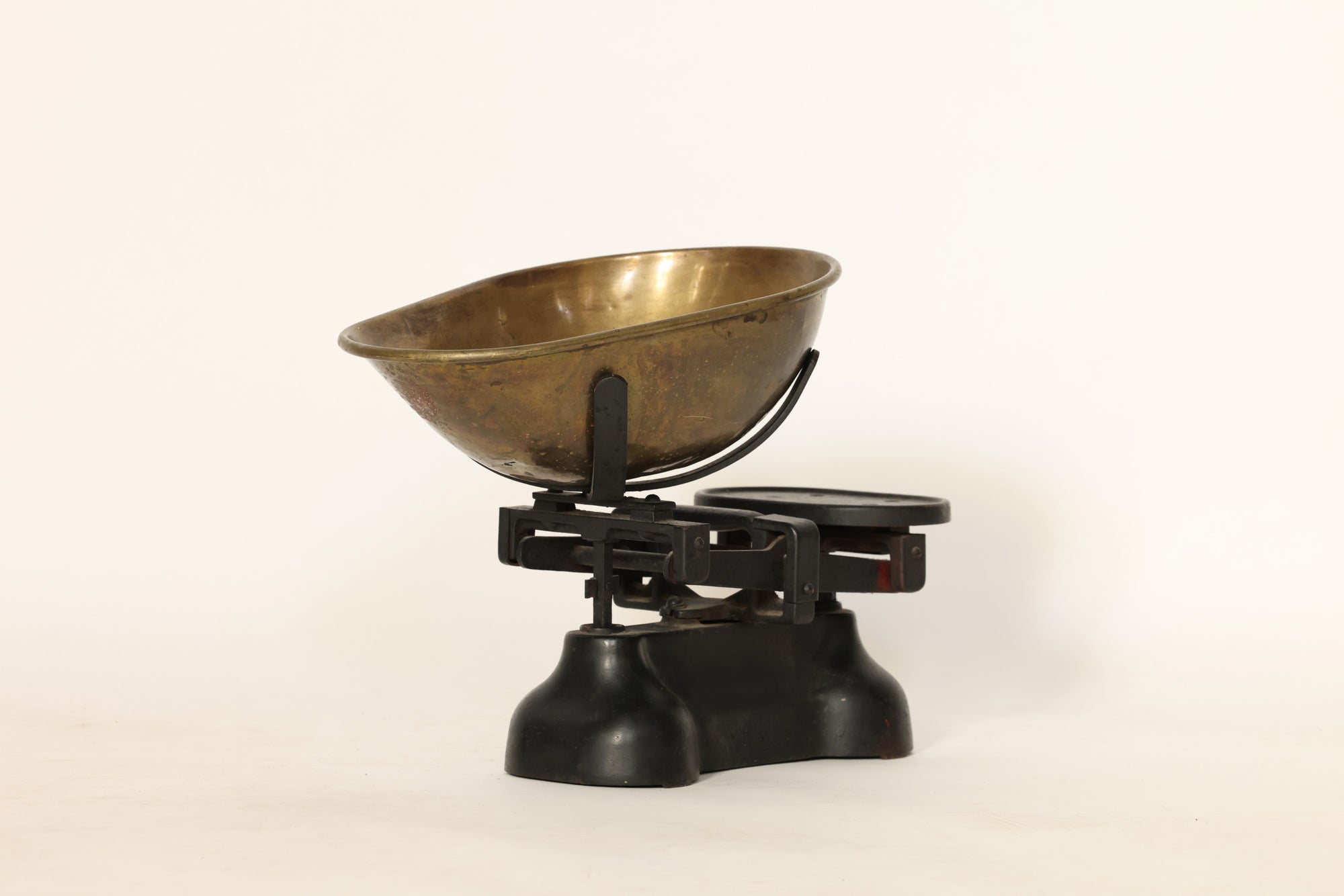 The Vintage Brass Balance Scale by Euro Trash Annie features a large brass bowl on one side and a flat metal platform on the other, all set on a black metal base against a plain white background.