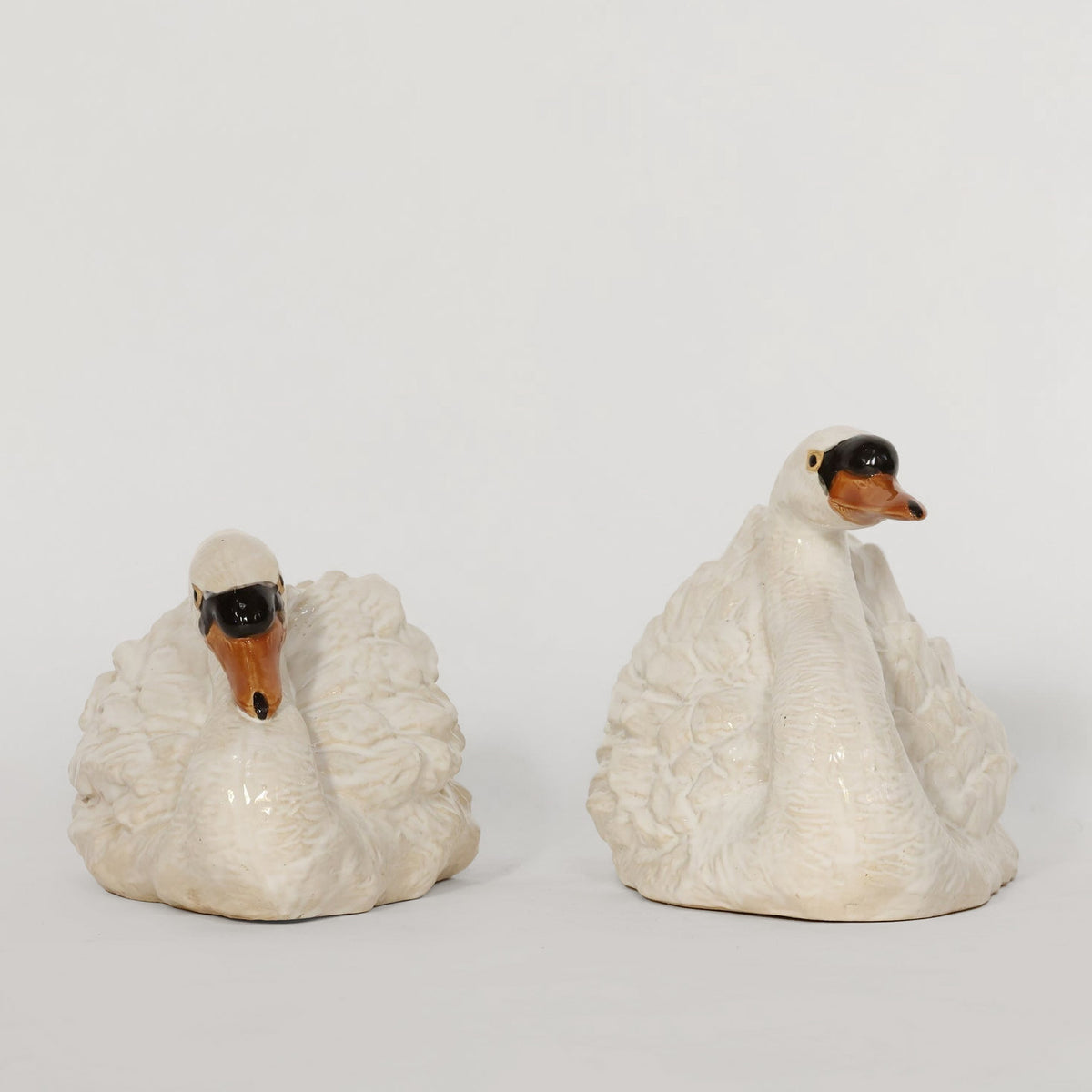 Two ceramic swan figures on a plain background