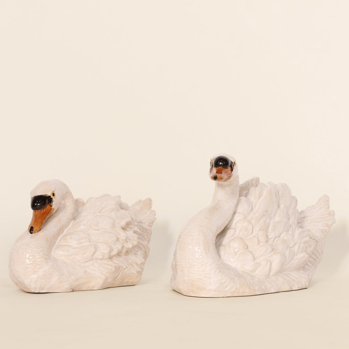 Two white ceramic swan figurines on a beige background