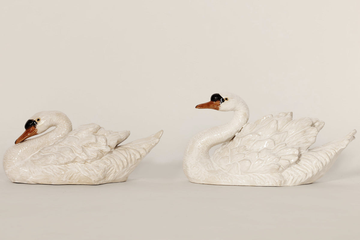 Two white ceramic swan figurines on a beige background