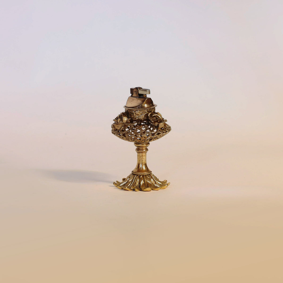 An exquisite Antique Gilt Brass Perfume Burner by Euro Trash Annie, featuring ornate floral filigree detailing, an elegant silhouette, and a decorative pedestal base—evoking the charm of a vintage gold metal table lighter and making a unique decorative accent against a plain light background.