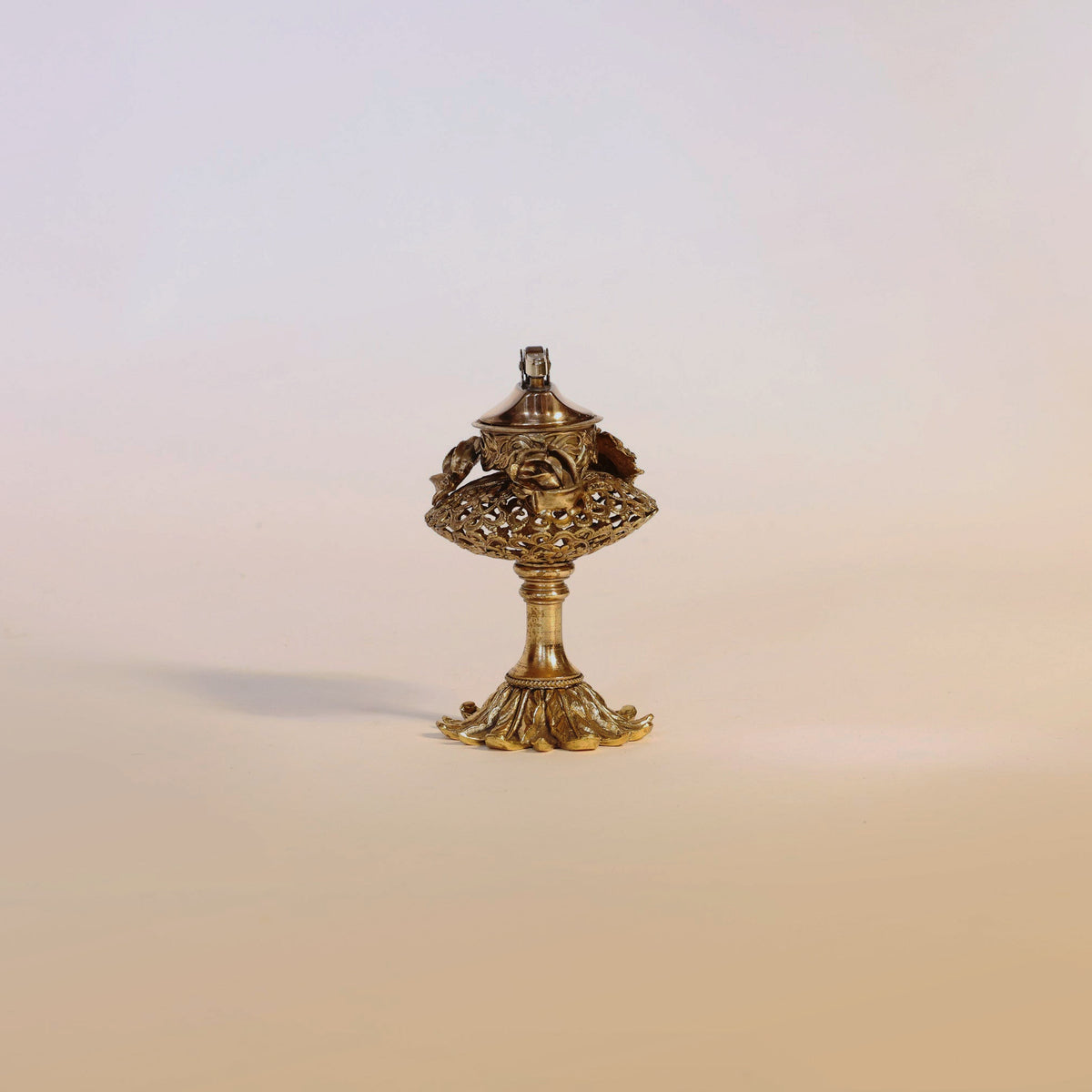 Centered against a plain, light background is the Antique Gilt Brass Perfume Burner by Euro Trash Annie—a small, ornate object featuring intricate designs. Its delicate silhouette and exquisite craftsmanship evoke the timeless charm of a decorative piece from another era.