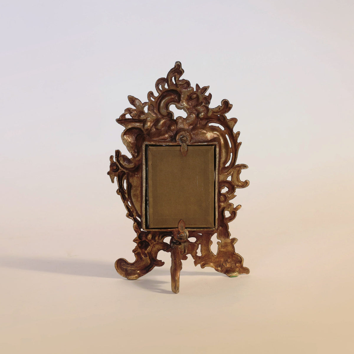 Euro Trash Annie “Antique Gilt Bronze Rococo Table Mirror” featuring ornate floral and scrollwork detailing in the Rococo style, standing on a single rear leg, displayed against a plain light background.