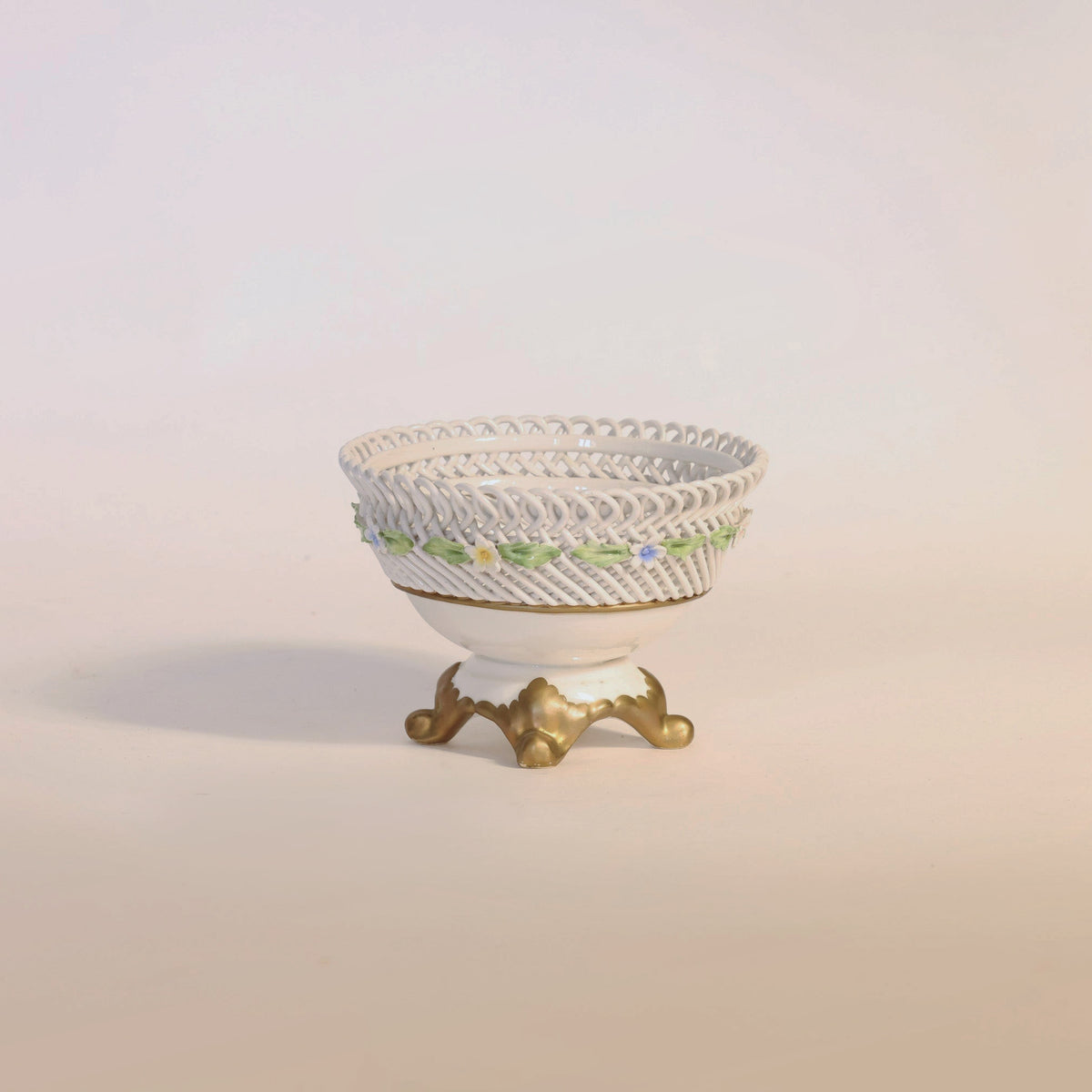 The Euro Trash Annie Antique Porcelain Reticulated Basket Compote features elegant pierced detailing, a lattice design, floral accents, and a gold-colored base, beautifully displayed against a plain light background.