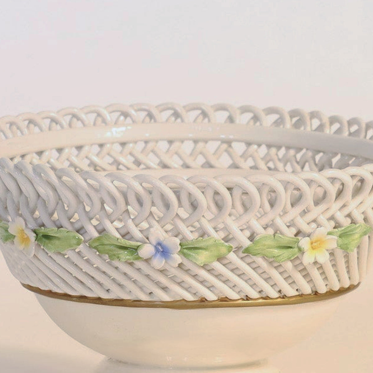 The Antique Porcelain Reticulated Basket Compote by Euro Trash Annie features a delicate open weave and pierced design, adorned with pastel-colored flowers and green leaves along the rim, and is showcased against a plain background.