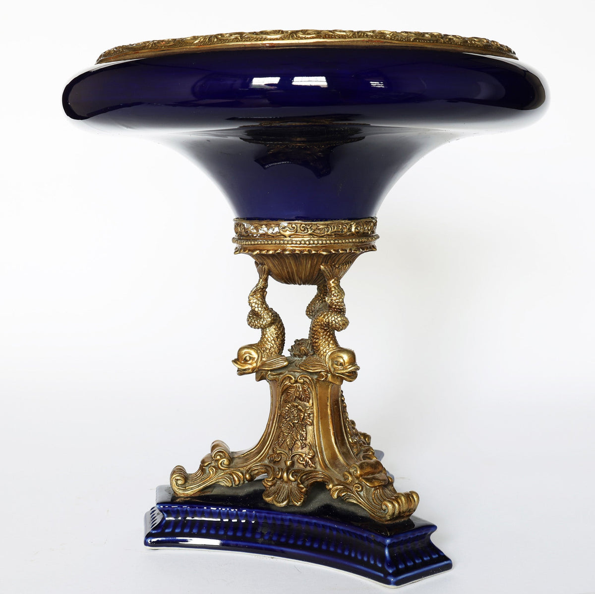 The Euro Trash Antique Cobalt Porcelain & Gilt Bronze Centerpiece Tazza features a deep blue porcelain top, ornate gilt bronze base with three sculpted dolphins, intricate details, and a matching cobalt and gold platform.
