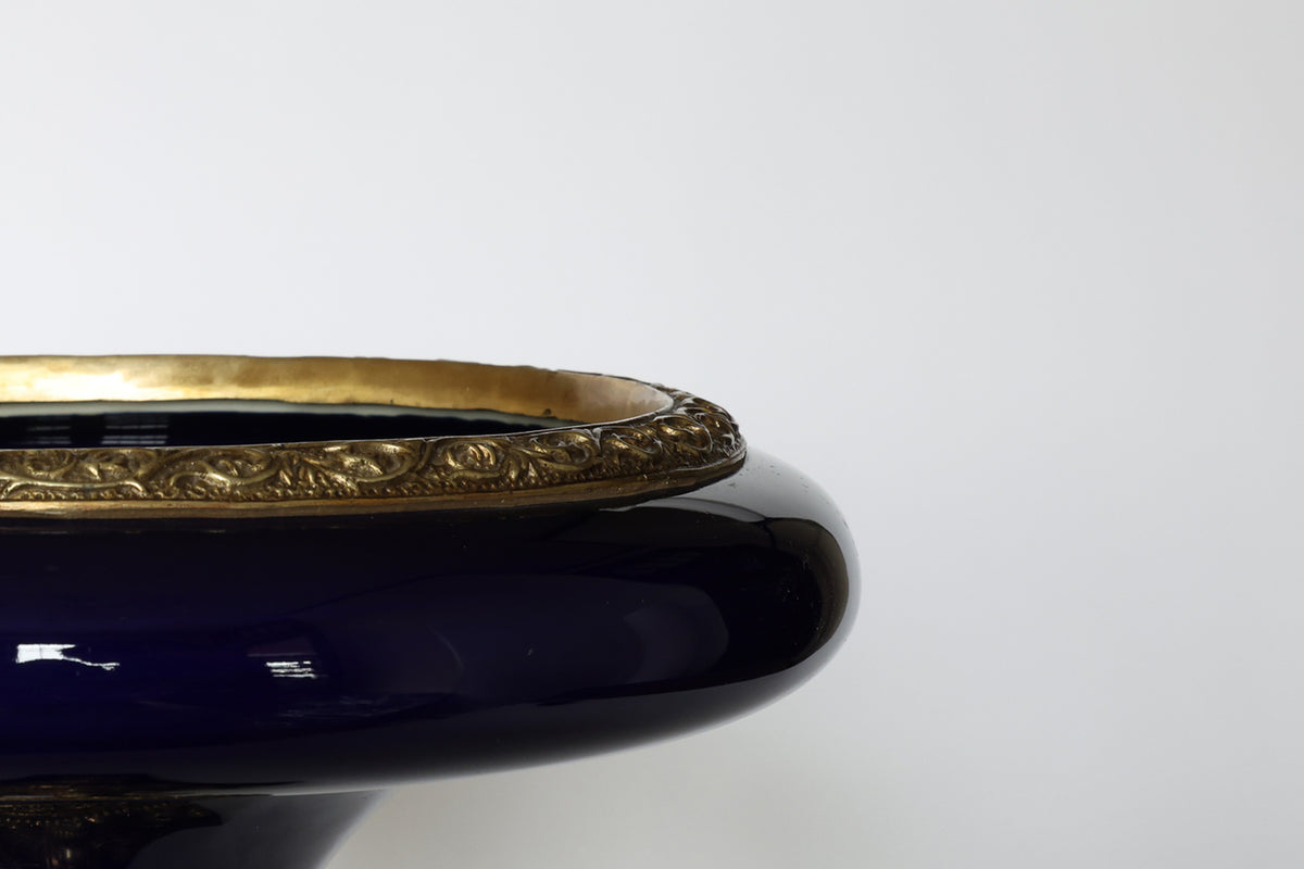 A close-up of the Euro Trash Antique Cobalt Porcelain & Gilt Bronze Centerpiece Tazza shows its glossy cobalt finish and decorative gold rim, with only part of the bowl visible on the left against a plain white background.