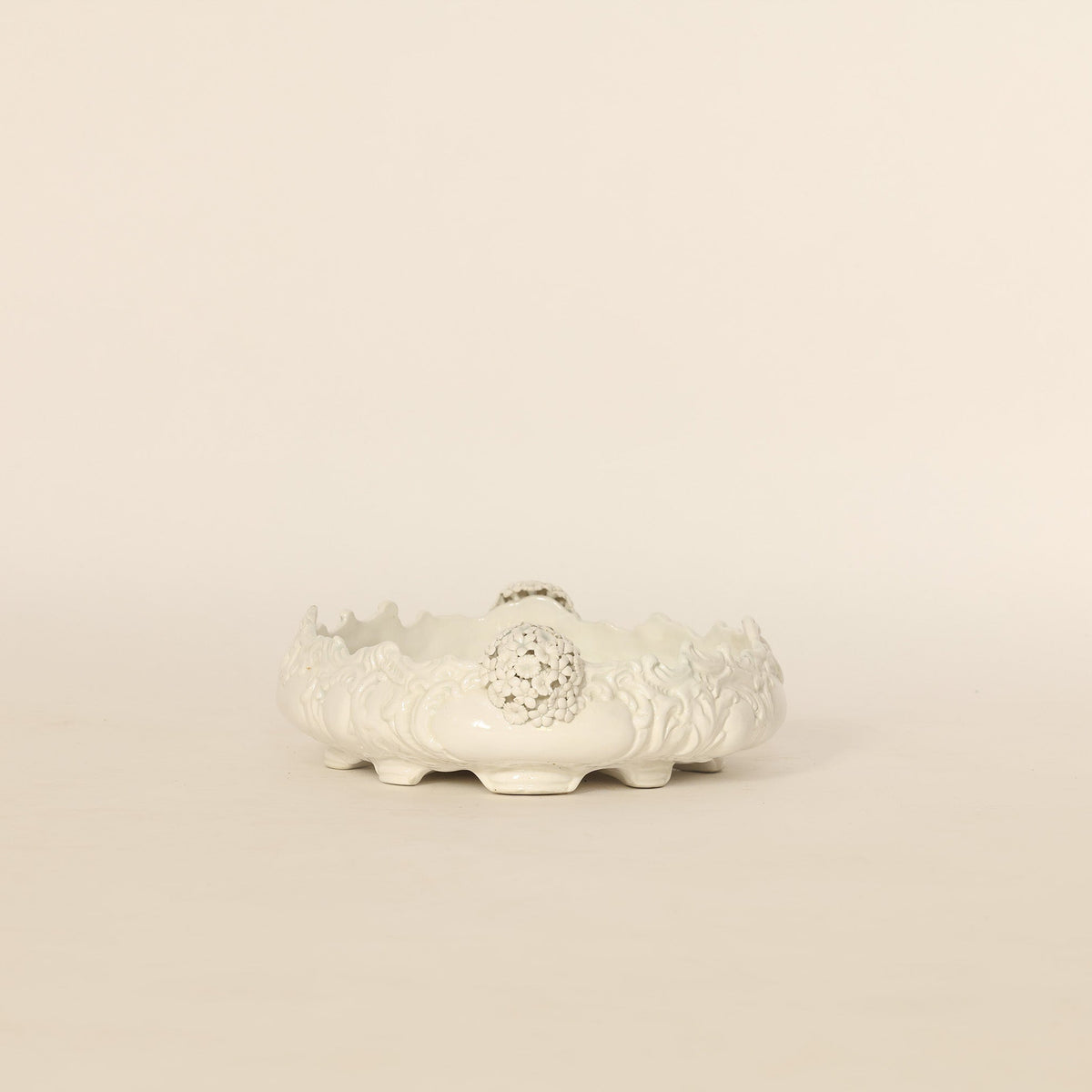 Decorative white ceramic pot with intricate designs on a beige background