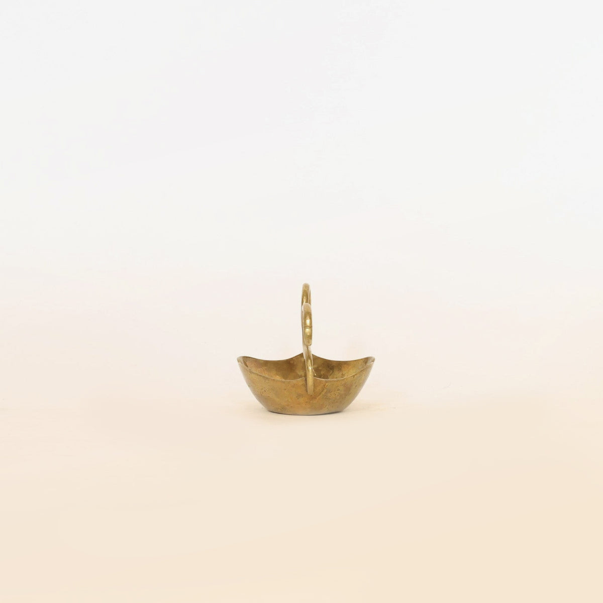 The Brass Swan Planter by Euro Trash Annie, with its petite golden brass form and elegant tall central handle, stands out as a striking sculptural accent against a plain, light background.