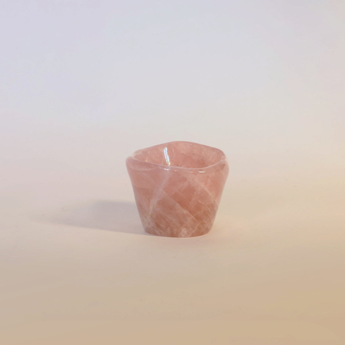 The Carved Rose Quartz Bowl from Euro Trash Annie makes an elegant decorative accent, its smooth surface sitting gracefully against a pale, neutral background.