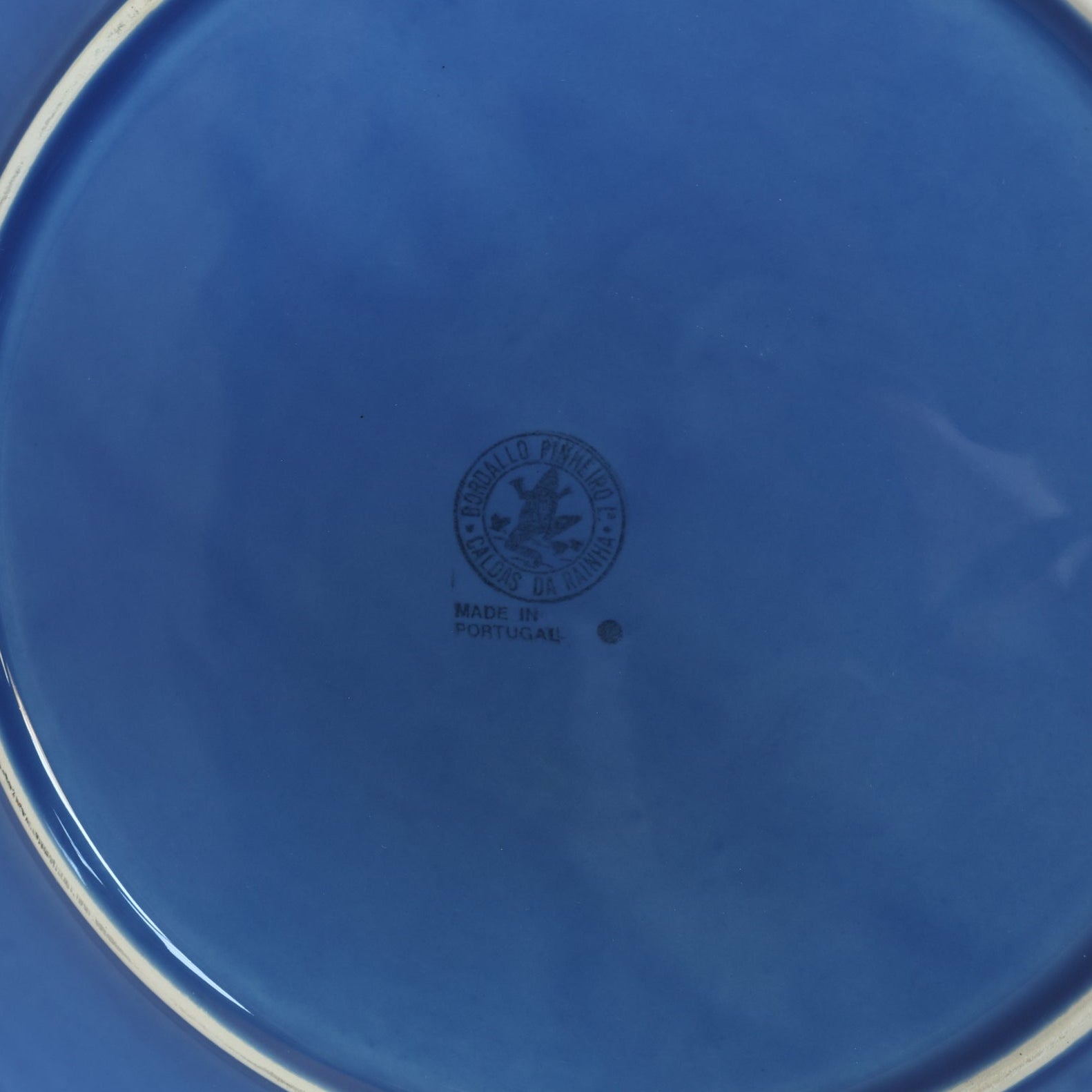 A close-up of the bottom of a Euro Trash Vintage Blue Rim Dinner Plate with a beaded edge, showing a black "Made in Portugal" stamp with an emblem—ideal for collectors of vintage dinnerware.