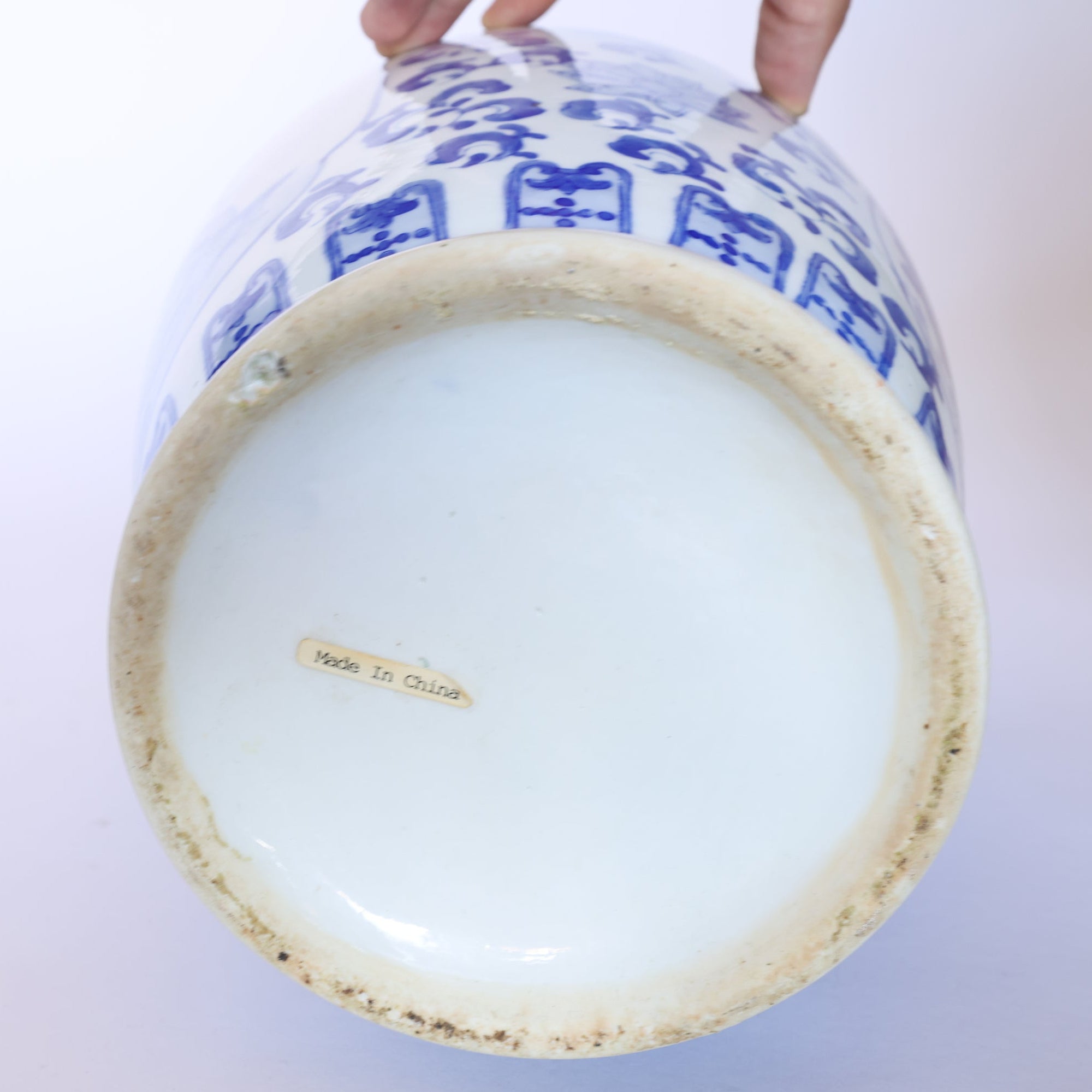 A hand holds the Euro Trash Vintage Blue & White Porcelain Peacock Vase, displaying its base with a small "Made In China" label and slightly worn, discolored edges.