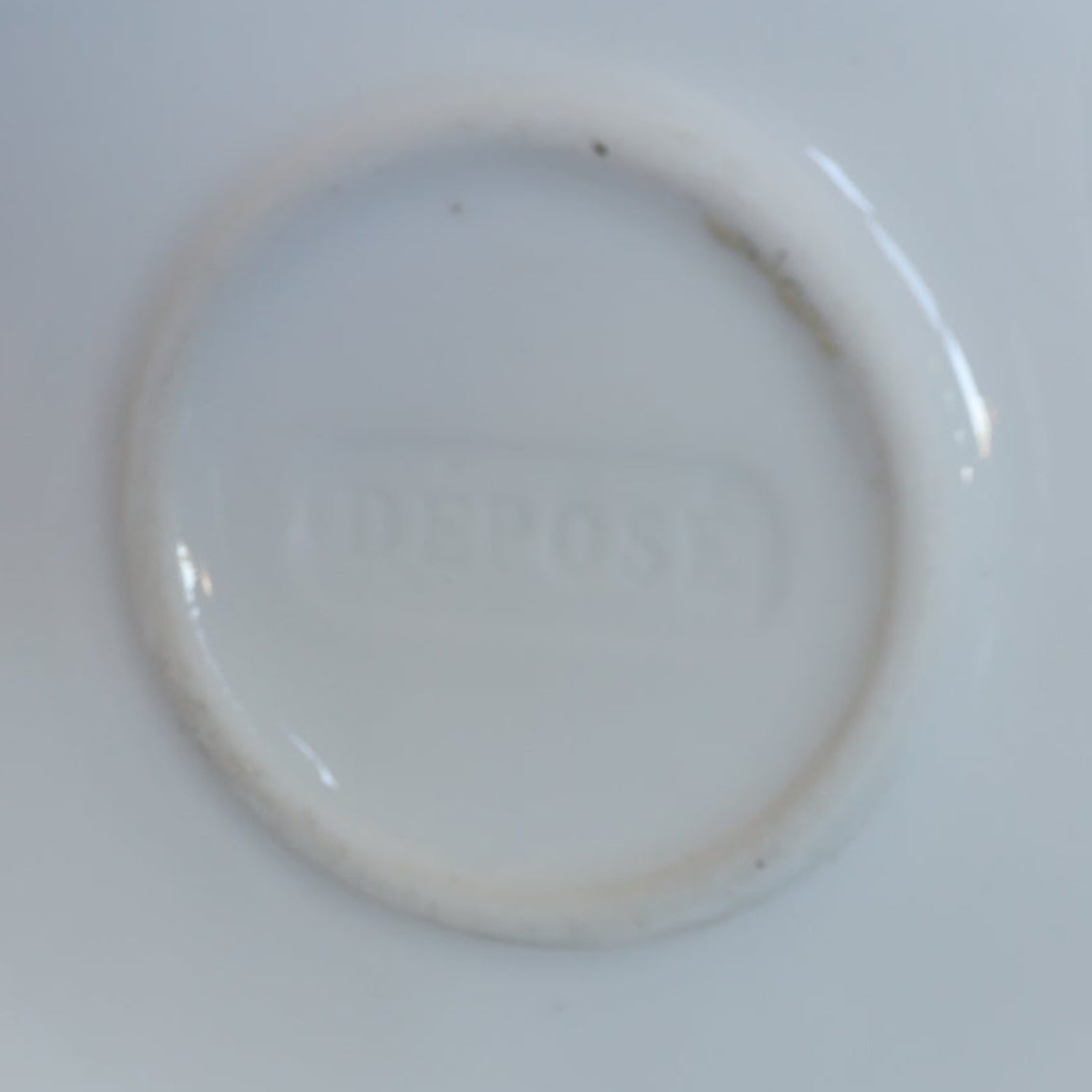 A close-up of the Vintage Blue Floral Porcelain Vase by Euro Trash highlights its white ceramic surface with an embossed circle and the word DEPOSE softly visible at the center.