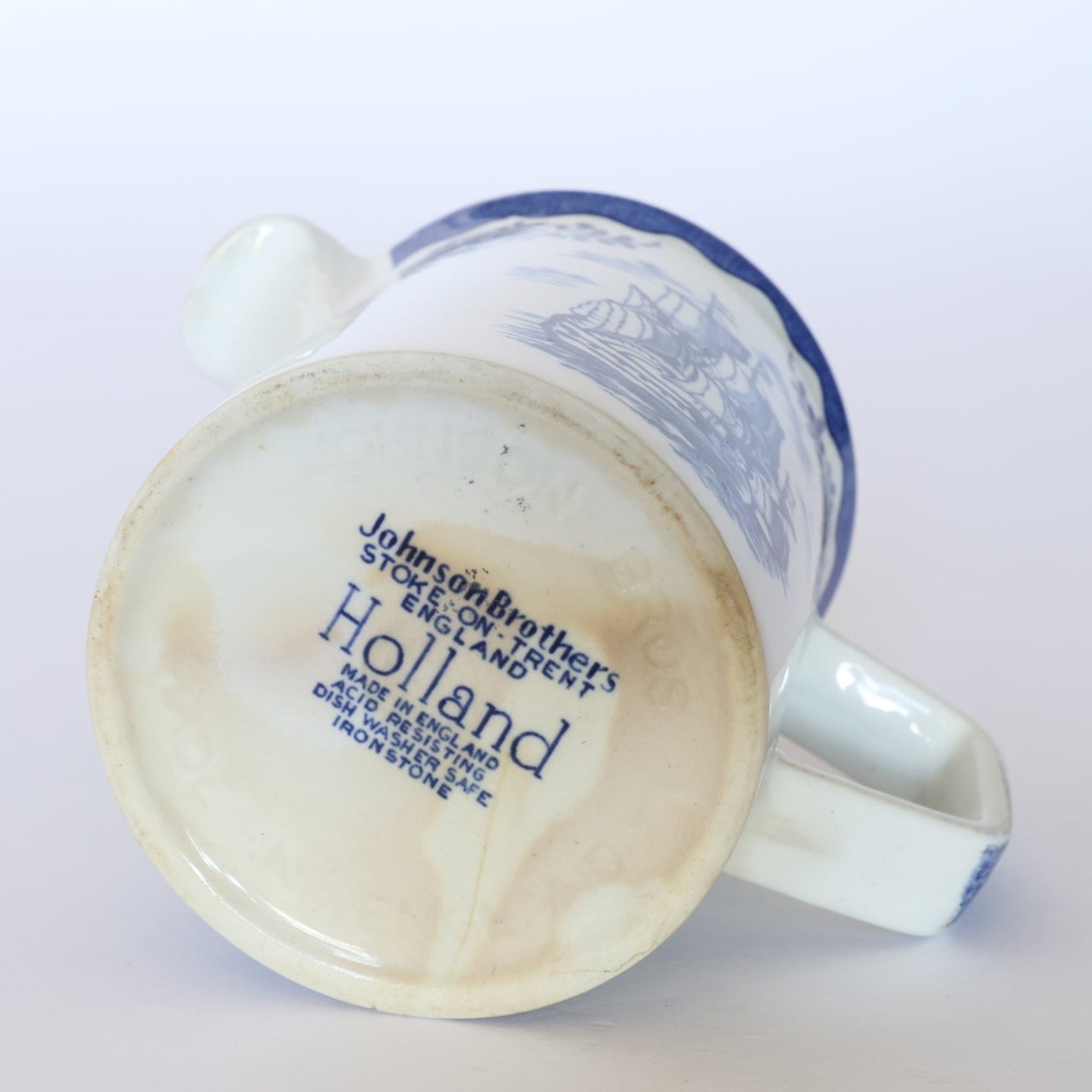 A Euro Trash Vintage Blue & White Ship Motif Porcelain Creamer lies on its side, displaying its brand stamp and nautical design with a blue rim, echoing classic maritime charm.