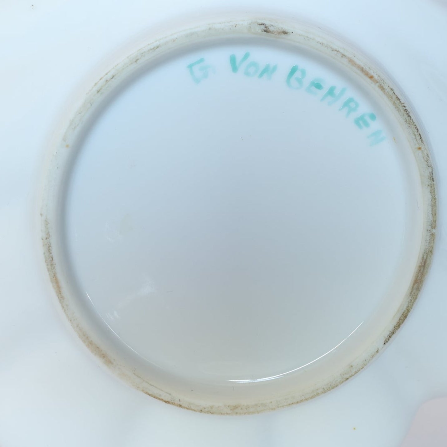 Bottom of a Euro Trash Vintage Hand-Painted Floral Porcelain Plate with gold rim, featuring "G. Von BeHREN" handwritten in light green ink near the base; rim shows slight discoloration.