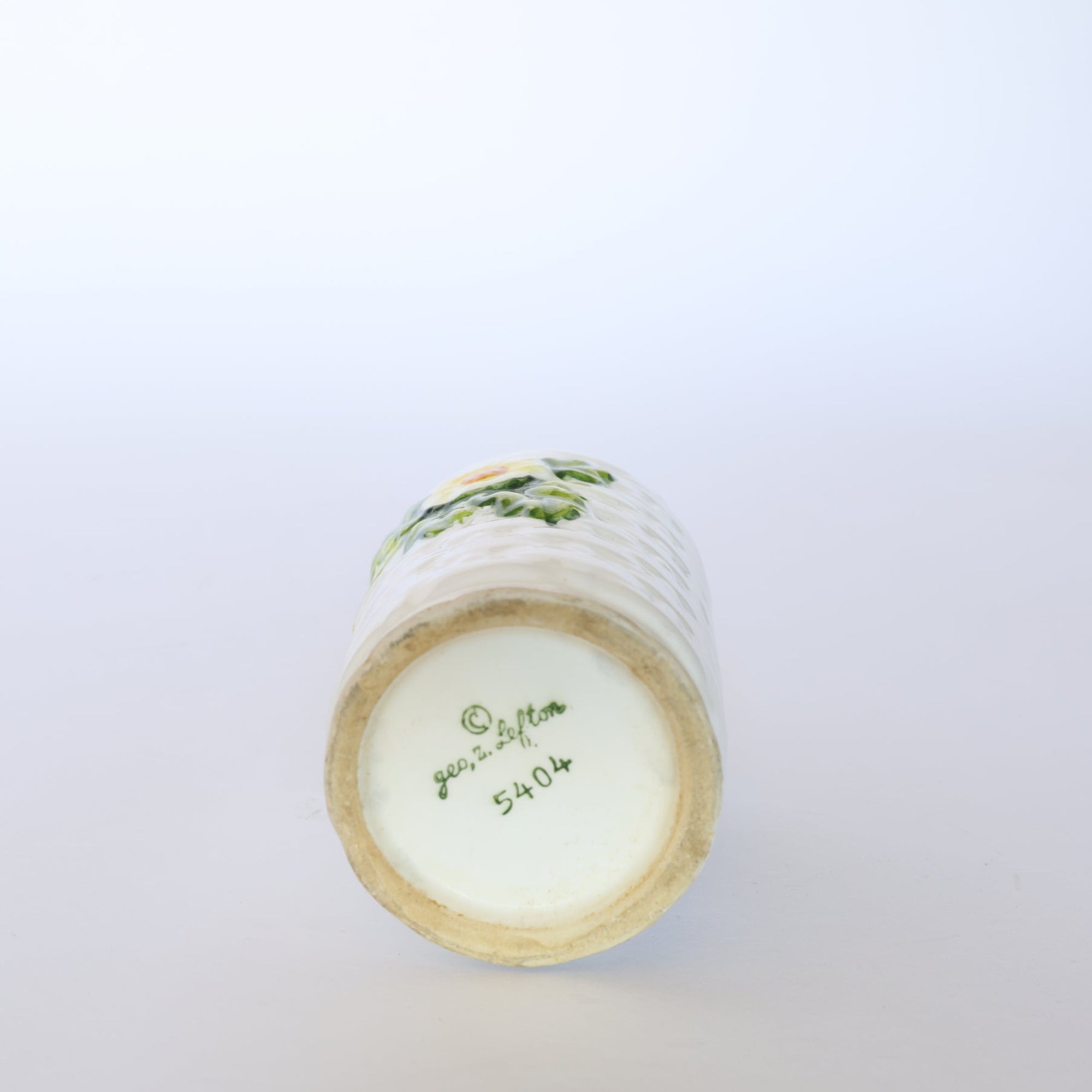 A Vintage Ivy Motif Ceramic Bud Vase by Euro Trash is shown lying on its side against a white background, displaying a base with handwritten green text reading “George Potton 5404” and a copyright symbol.