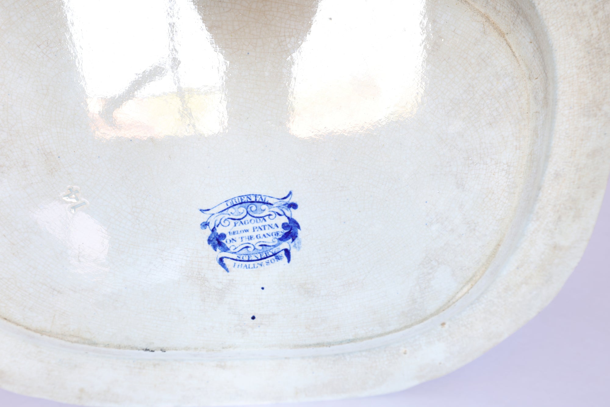 The bottom of the Vintage Blue & White Floral Transferware Serving Platter by Euro Trash features a blue maker's mark. Its decorative border and crackled glaze add classic charm inspired by traditional designs.