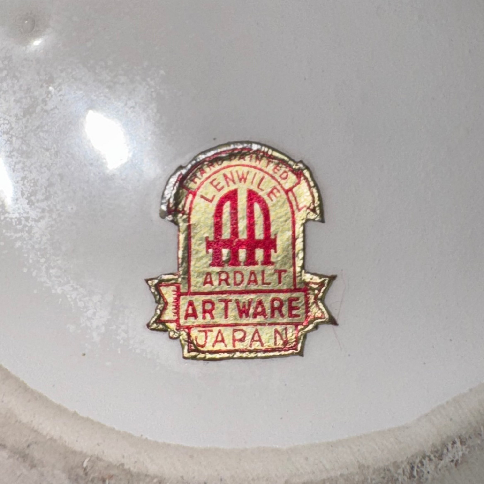 Close-up of a metallic sticker label with red and gold text reading Euro Trash Annie affixed to glossy white Pair of Porcelain Cherub Figurines—ideal for collectors of vintage home decor.