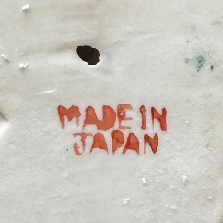 The Euro Trash Annie Vintage Porcelain Dog & Puppy Figurine features “MADE IN JAPAN” cut from a rough, white textured base with red showing through, plus a hole and marks above the text—ideal for nostalgic home decor collectors.