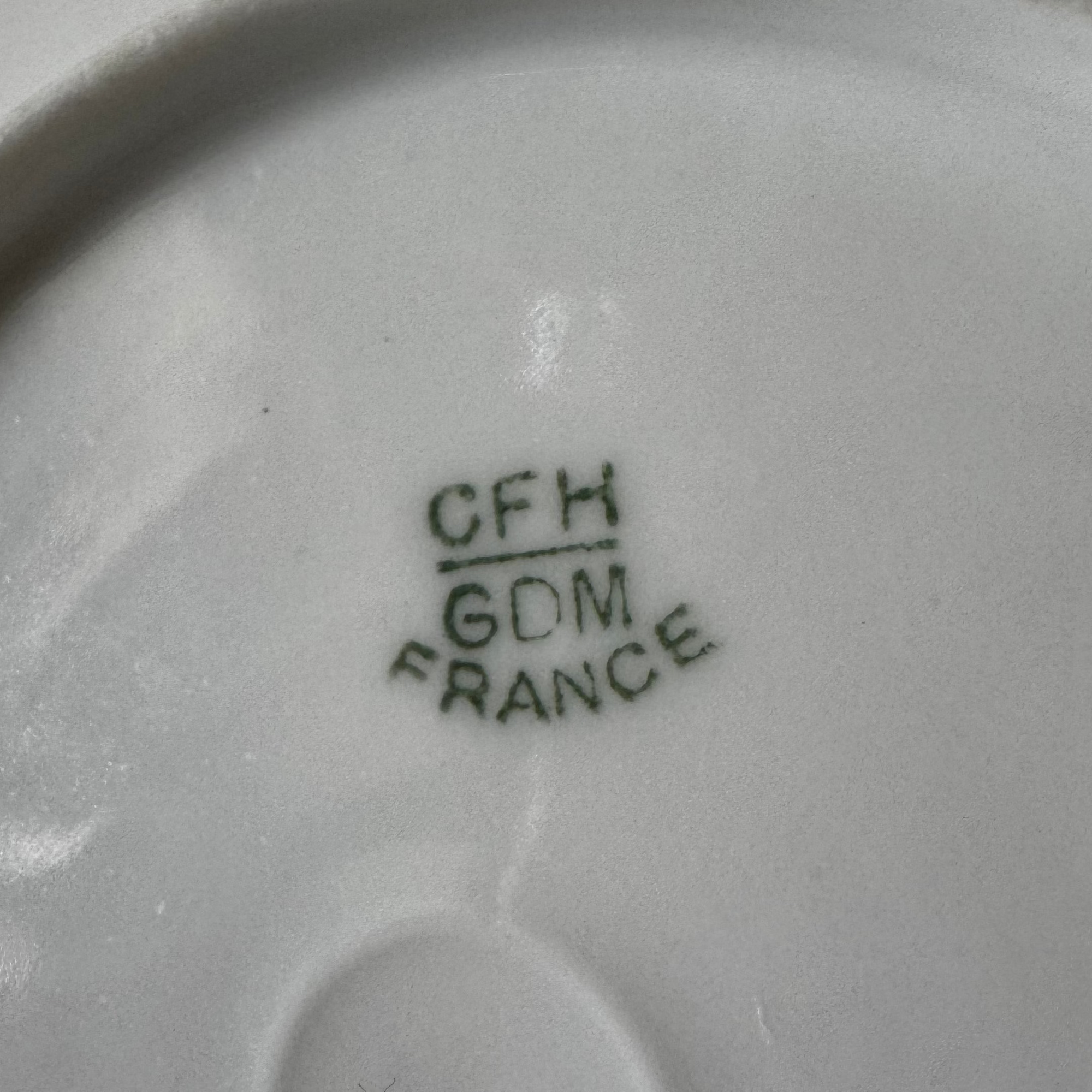 Close-up of a Euro Trash Vintage White Embossed Rim Ceramic Bowl showing its white surface and a green maker's mark with CFH / GDM FRANCE printed in three lines.