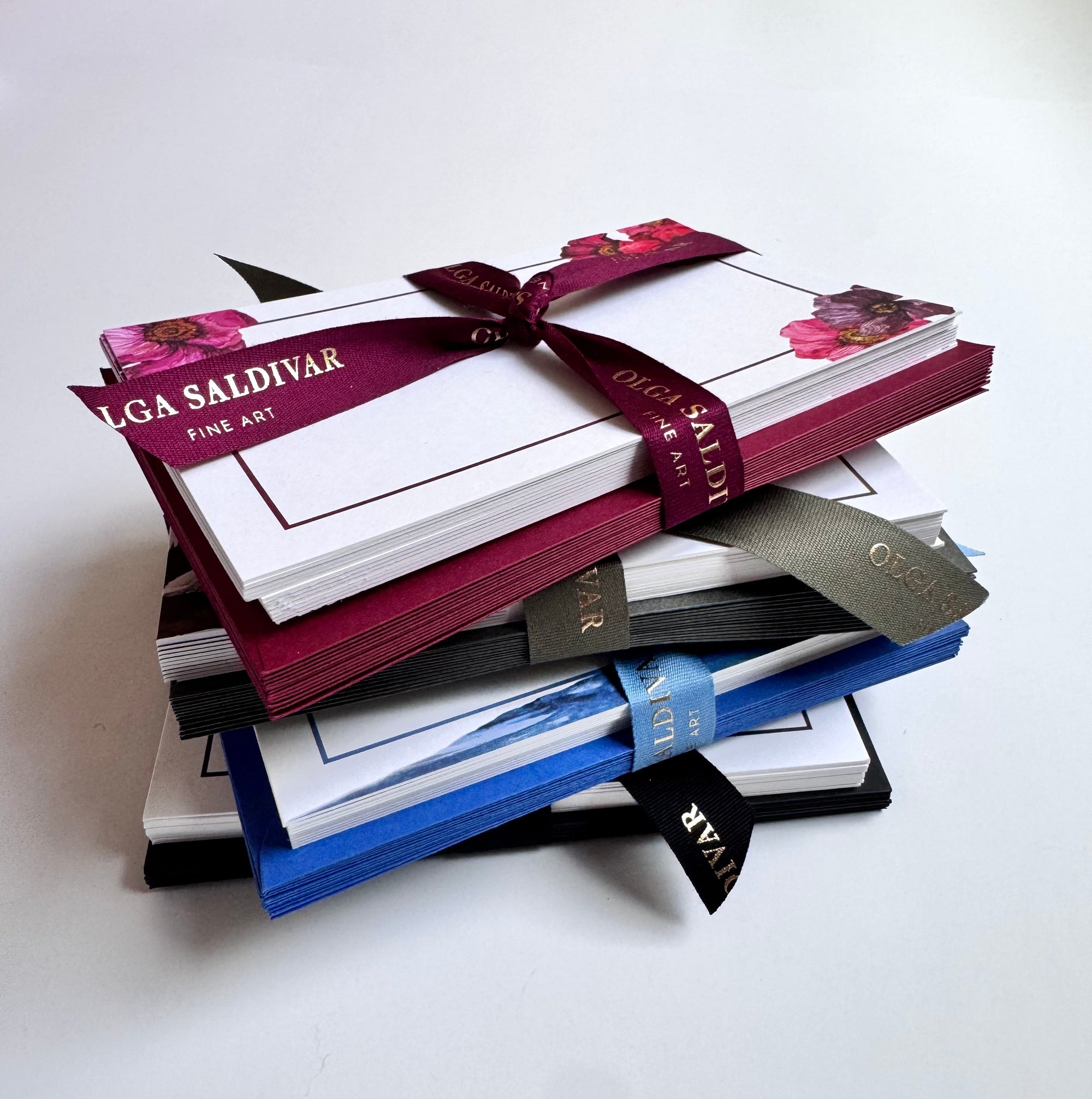 A stack of notecards tied with burgundy, black, and blue ribbons—featuring floral and scenic designs from the Blue Reverie Stationery Set by Euro Trash Annie—shown on a white background.
