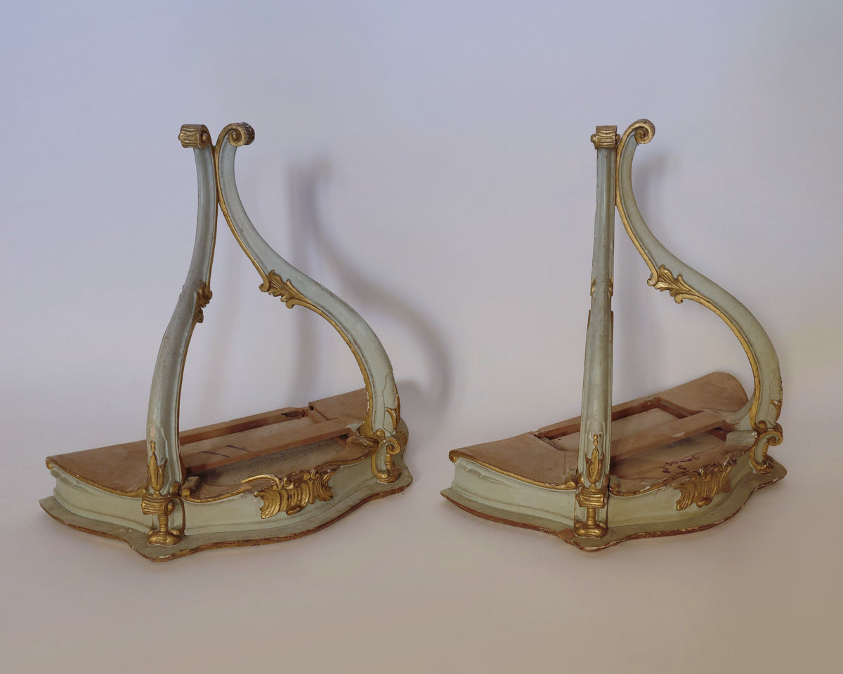 A pair of vintage giltwood wall corbels by Euro Trash Annie, featuring ornate curved wooden frames with gold accents, are positioned on their sides against a plain background. Reminiscent of antique furniture bases—possibly from chairs or tables—these unique pieces make striking architectural decor.