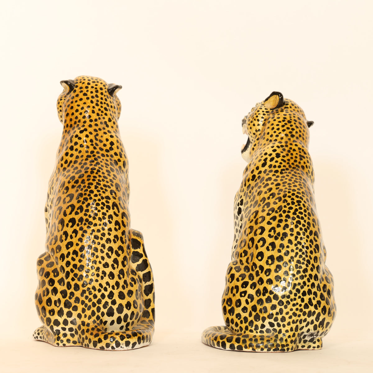Two ceramic cheetah figurines on a beige background