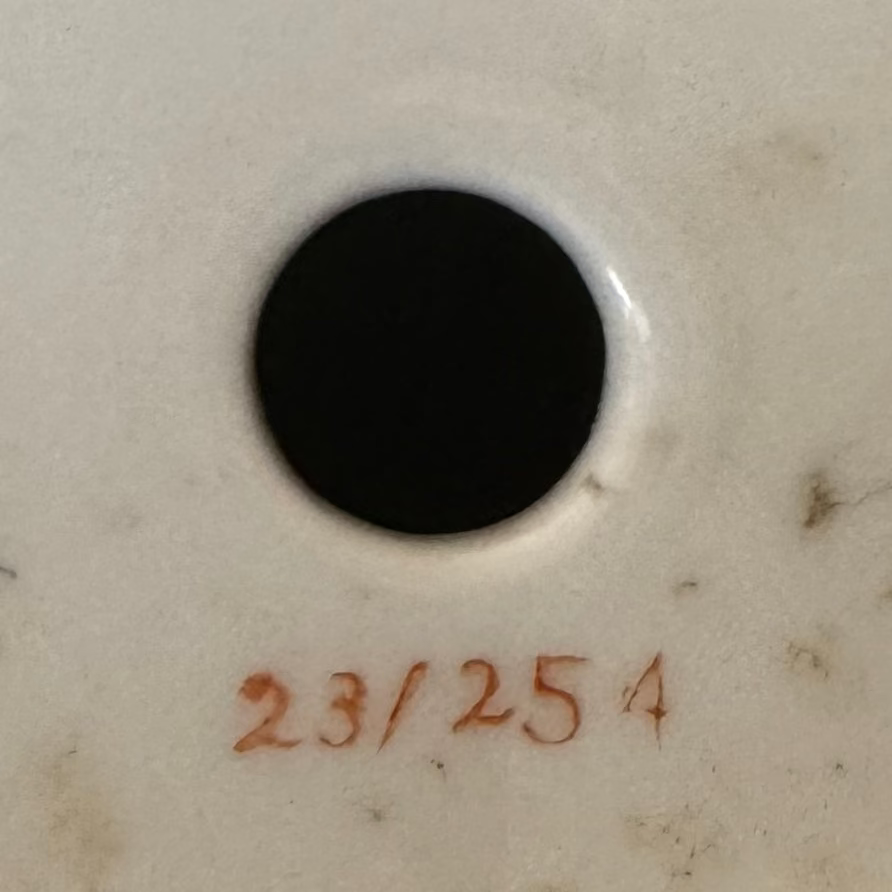 A black circle centered on white with “23/254” in reddish-brown evokes the refined gilt detailing of the Pair of Gilt & Porcelain Dancing Figures by Euro Trash Annie.