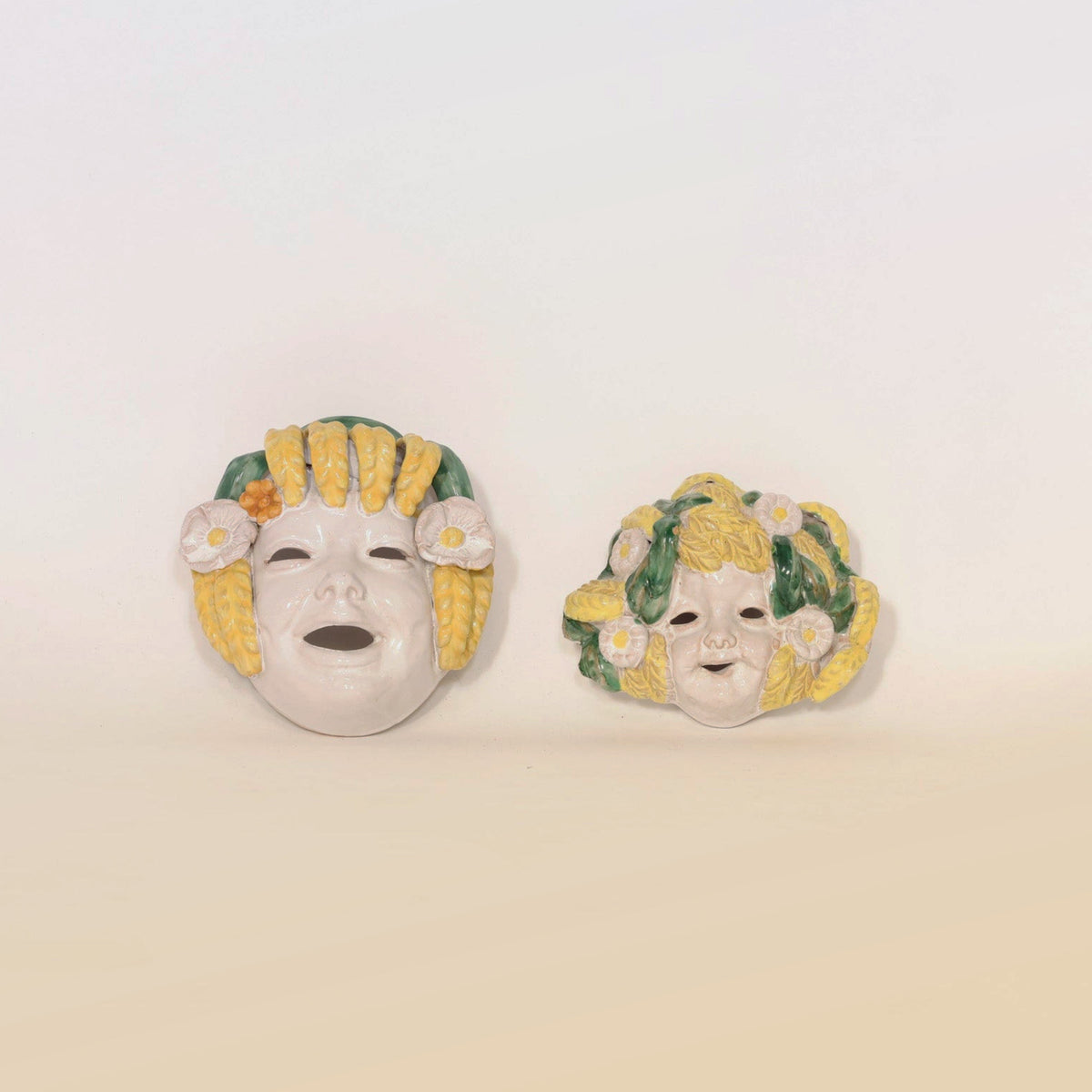 Add a visually stunning touch to your home with the Pair of Italian Majolica Figural Wall Masks by Euro Trash Annie. This artisanal duo features two ceramic masks with yellow hair adorned with delicate white flowers and leaf accents. The left mask captivates with its open mouth and eyes, providing a striking contrast to the right mask’s gentle smile and closed eyes. Both pieces highlight the timeless elegance of Italian majolica craftsmanship, making them a unique statement in figural wall art décor.
