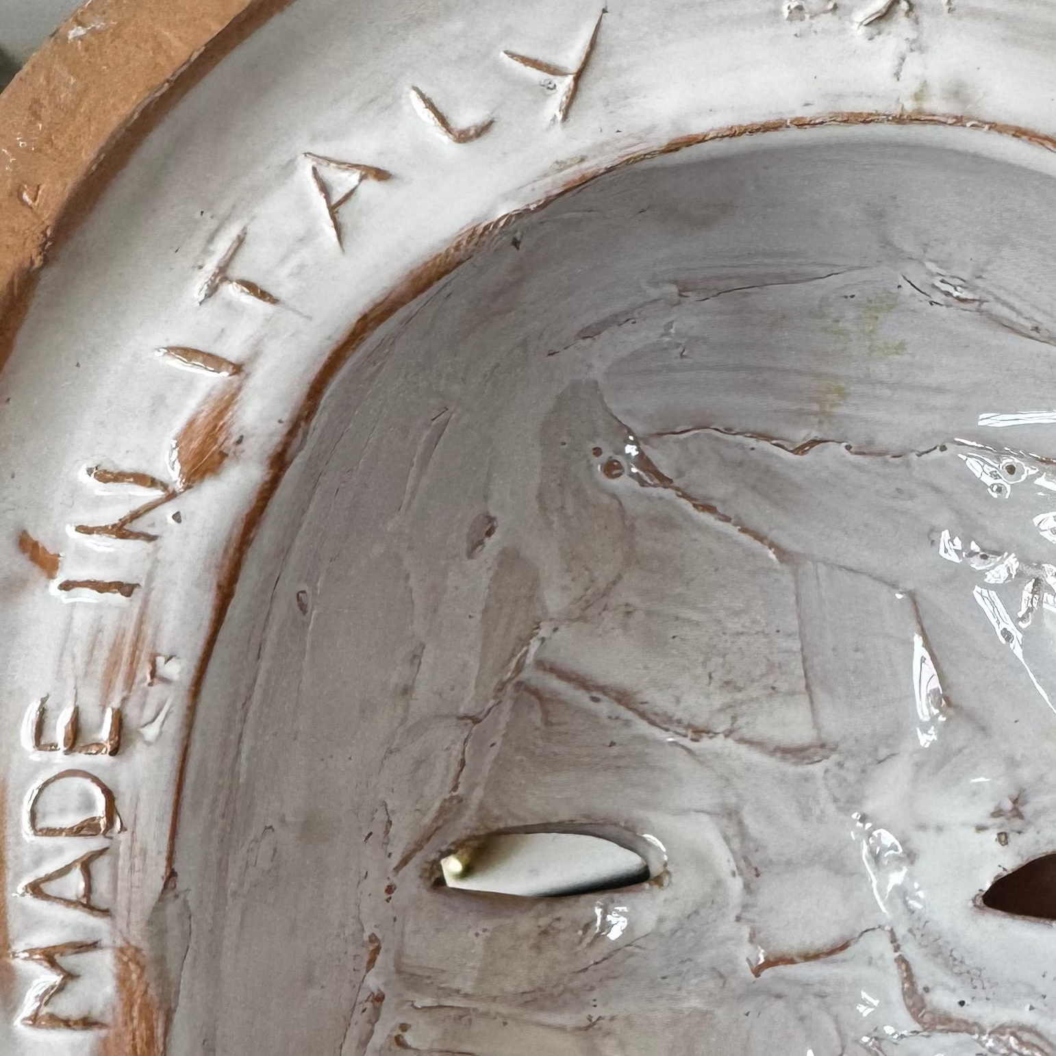 Close-up of the inner rim of a Euro Trash Annie Pair of Italian Majolica Figural Wall Masks, showing raised MADE IN ITALY text, glossy light glaze, and two eye holes.
