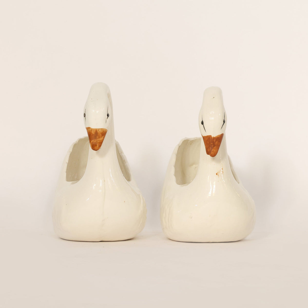 Two swan shaped ceramic figurines on a light background