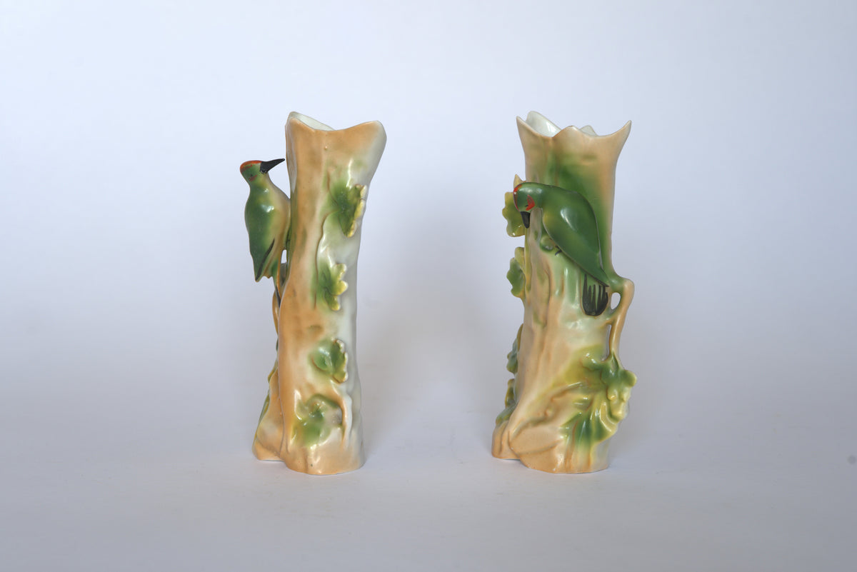 Pair of Vintage Ceramic Hand-Painted Bird Vases by Euro Trash—tree trunk-shaped with glossy finish, each featuring a hand-painted green woodpecker. These soft cottage-style pieces are shown against a plain white background.