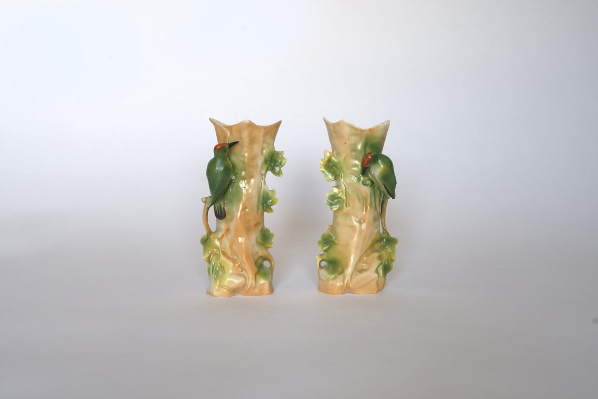 The Euro Trash Pair of Vintage Ceramic Hand-Painted Bird Vases showcases beige bases, green leafy details, and perched green birds with red heads—perfect for adding cottage charm to any white backdrop.