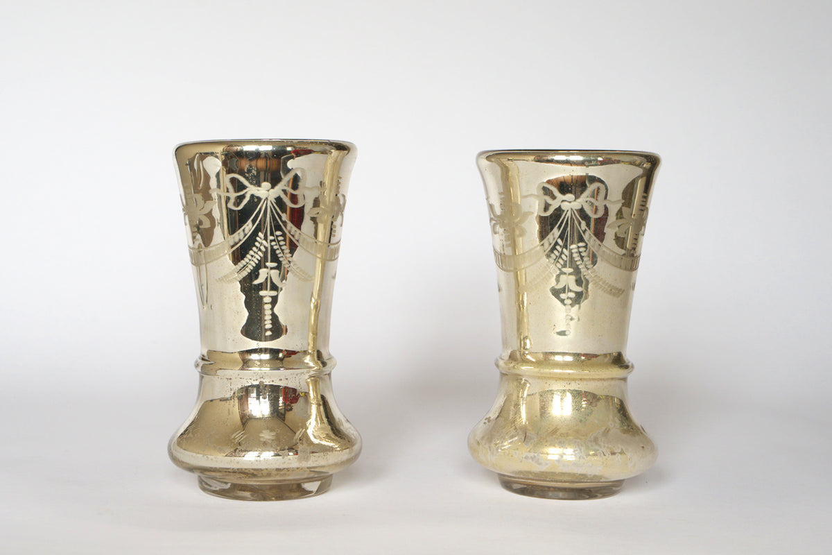 The Pair of Vintage Etched Mercury Glass Vases by Euro Trash features two silver-toned vases with etched garland motifs and flared tops, shown side by side against a plain white background.