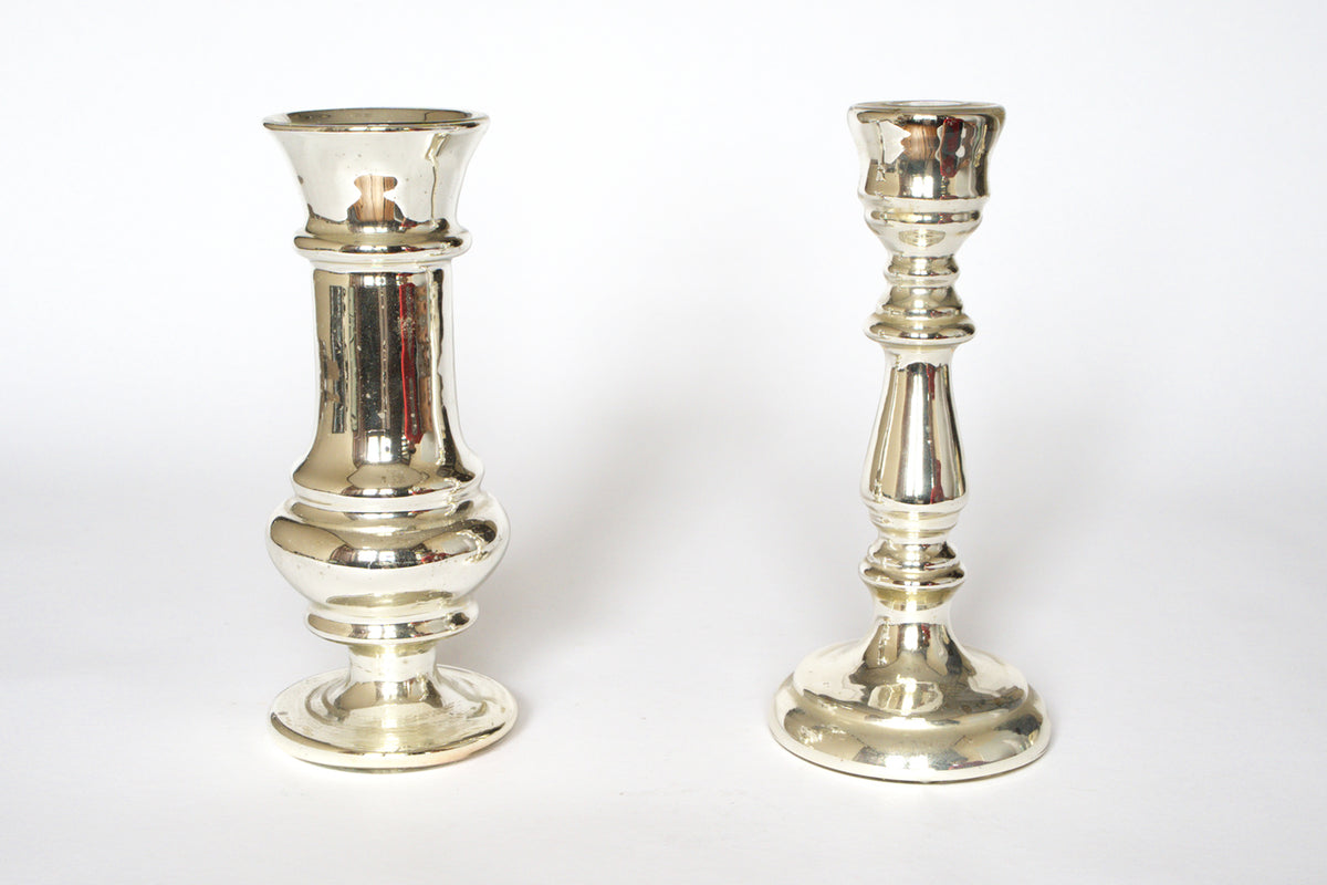 A pair of Vintage Mercury Glass Candleholders by Euro Trash stands upright on a white background. The left candleholder is taller with a wider base, while the right one is shorter and slimmer. Both feature a reflective silvered finish.