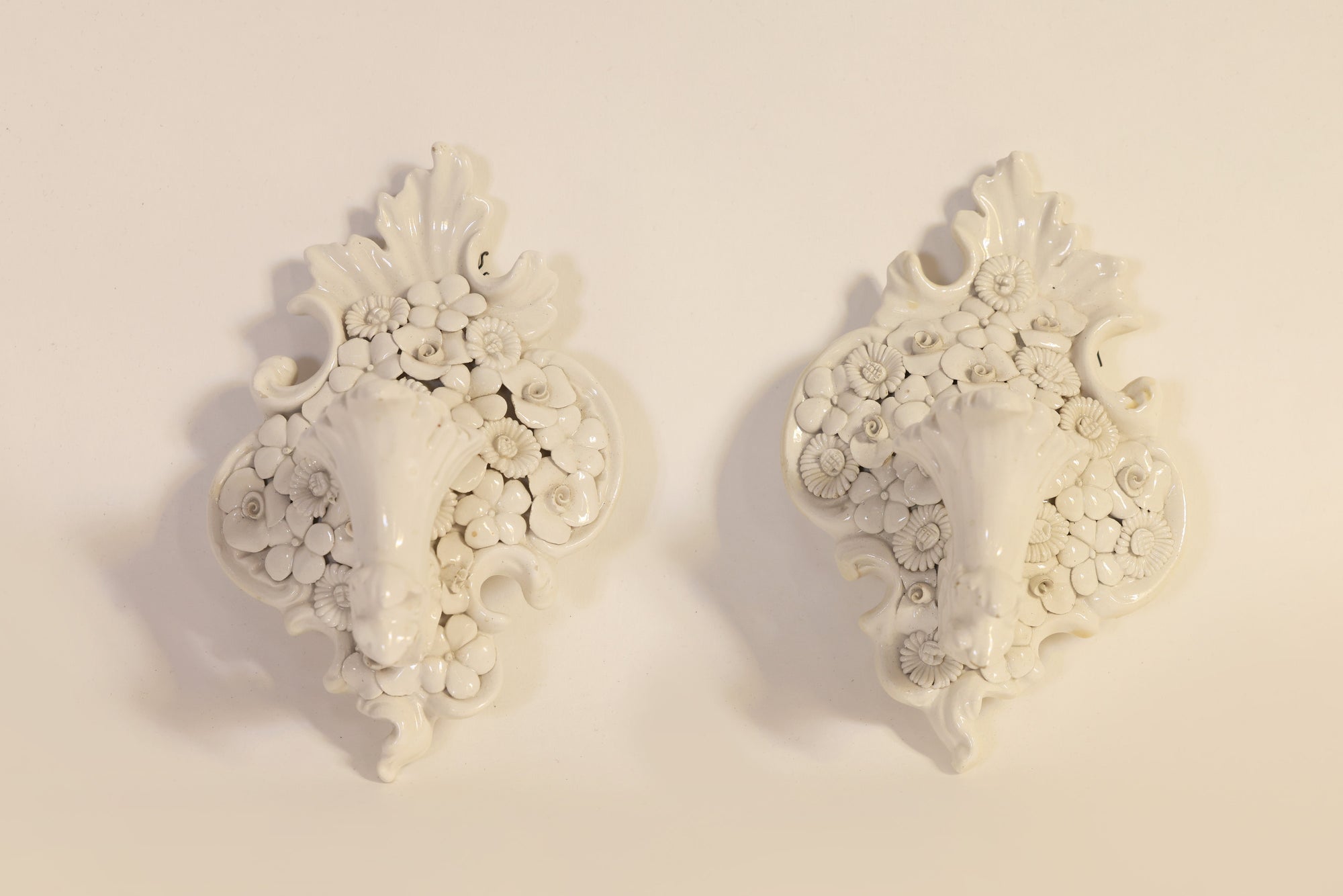 The Pair of Porcelain Floral Wall Pocket Vases by Euro Trash features ornate white designs with intricate floral patterns and cornucopia motifs, displayed side by side to evoke the elegance of vintage wall decor.